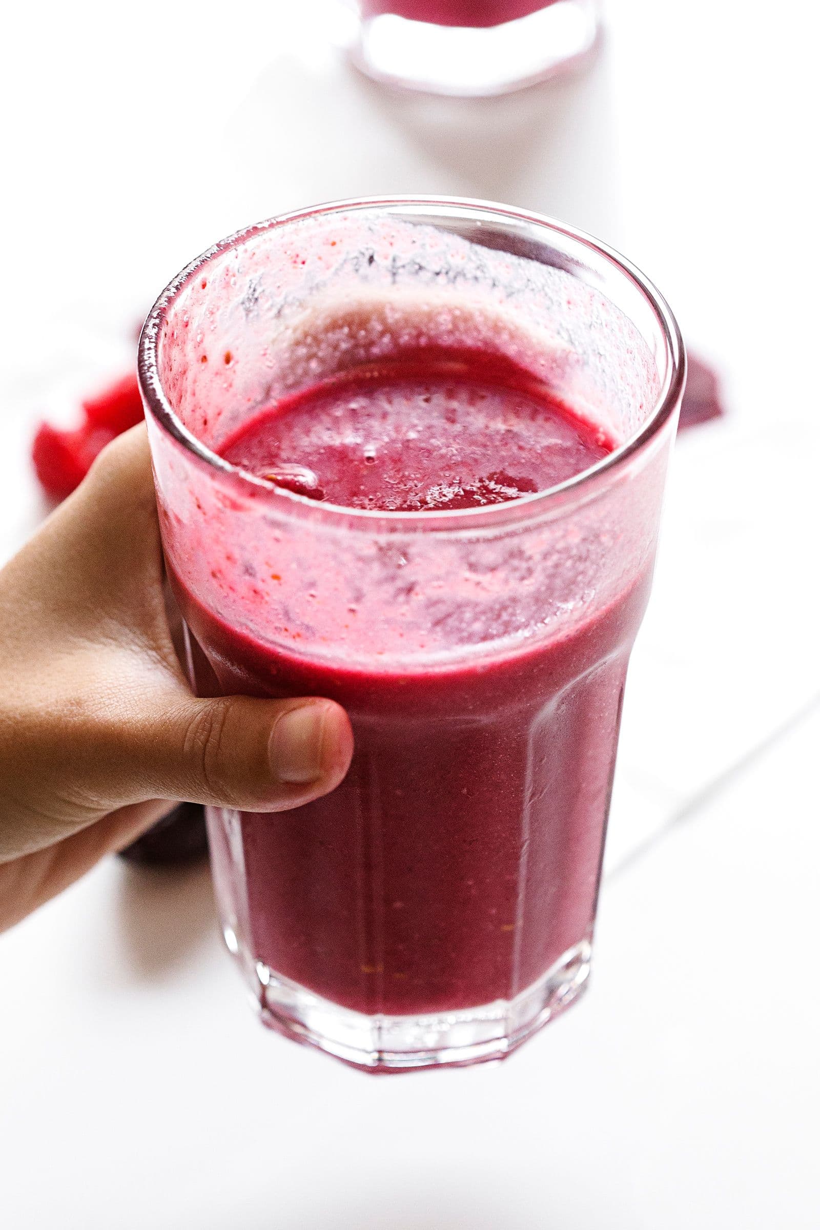 Mão a segurar um copo cheio de smoothie de beterraba e framboesa sobre fundo branco.