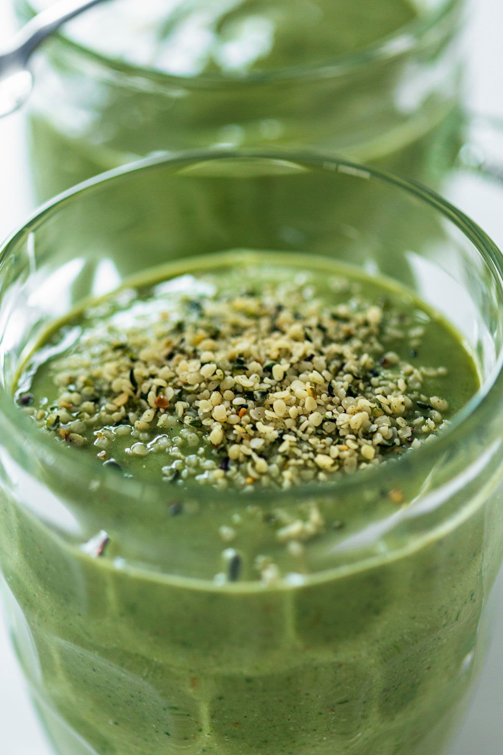 Thick green smoothie topped with hemp seeds in a glass mug.