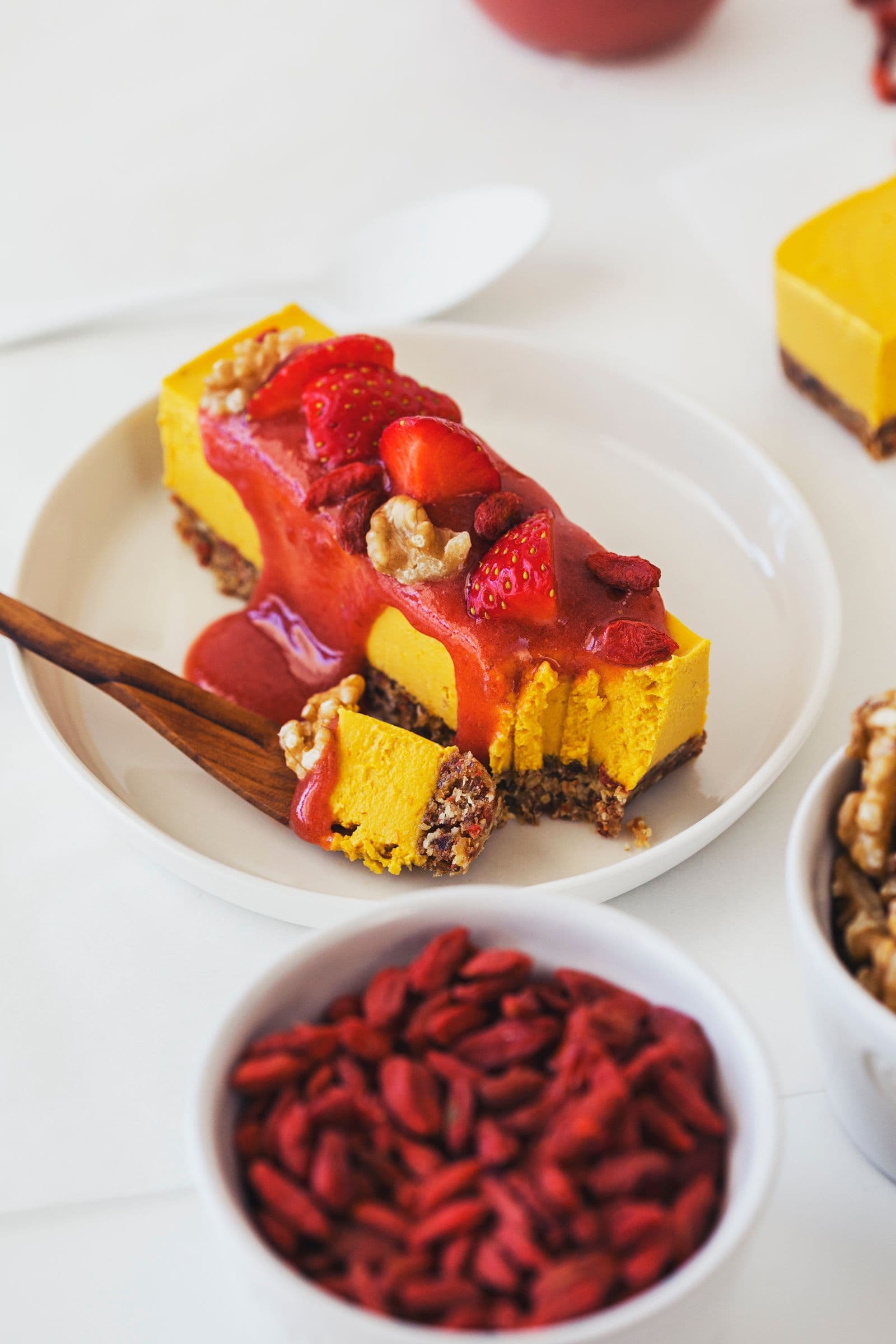 Beautifully decorated raw vegan cheesecake on a small, white dish with a wooden fork.