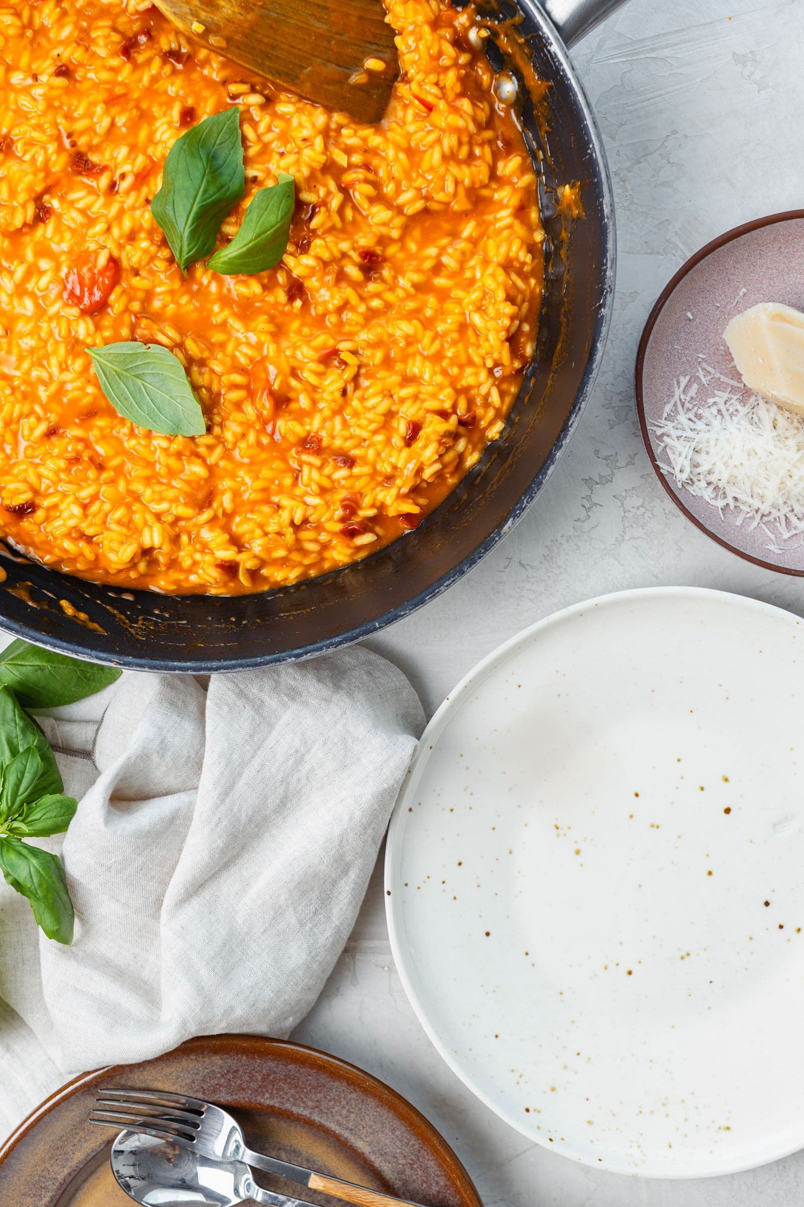 Risotto de tomate numa frigideira grande, coberto com folhas de manjericão fresco, pronto a servir.