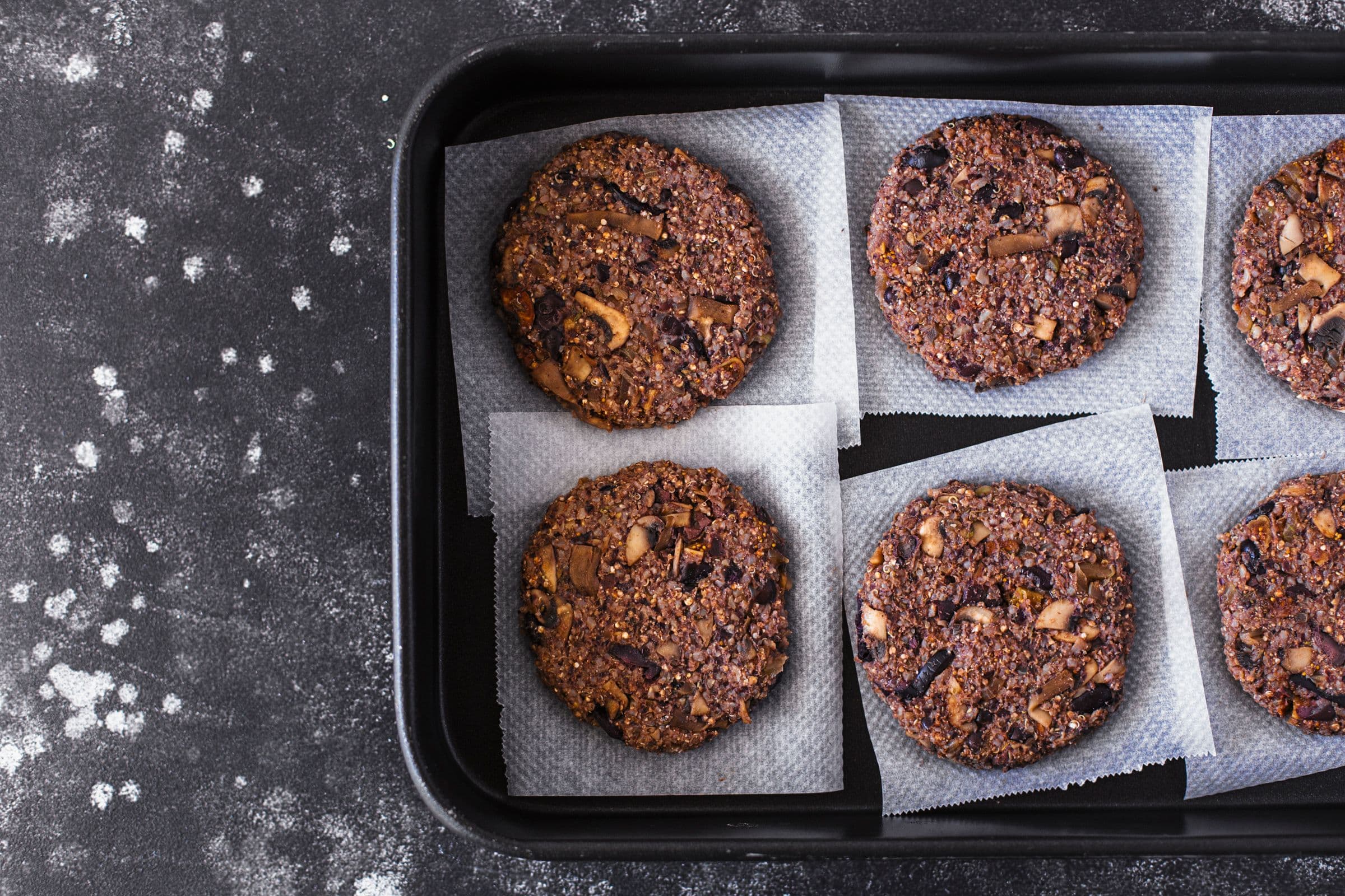 Uncooked burger patties neatly arranged on a parchment-lined tray.