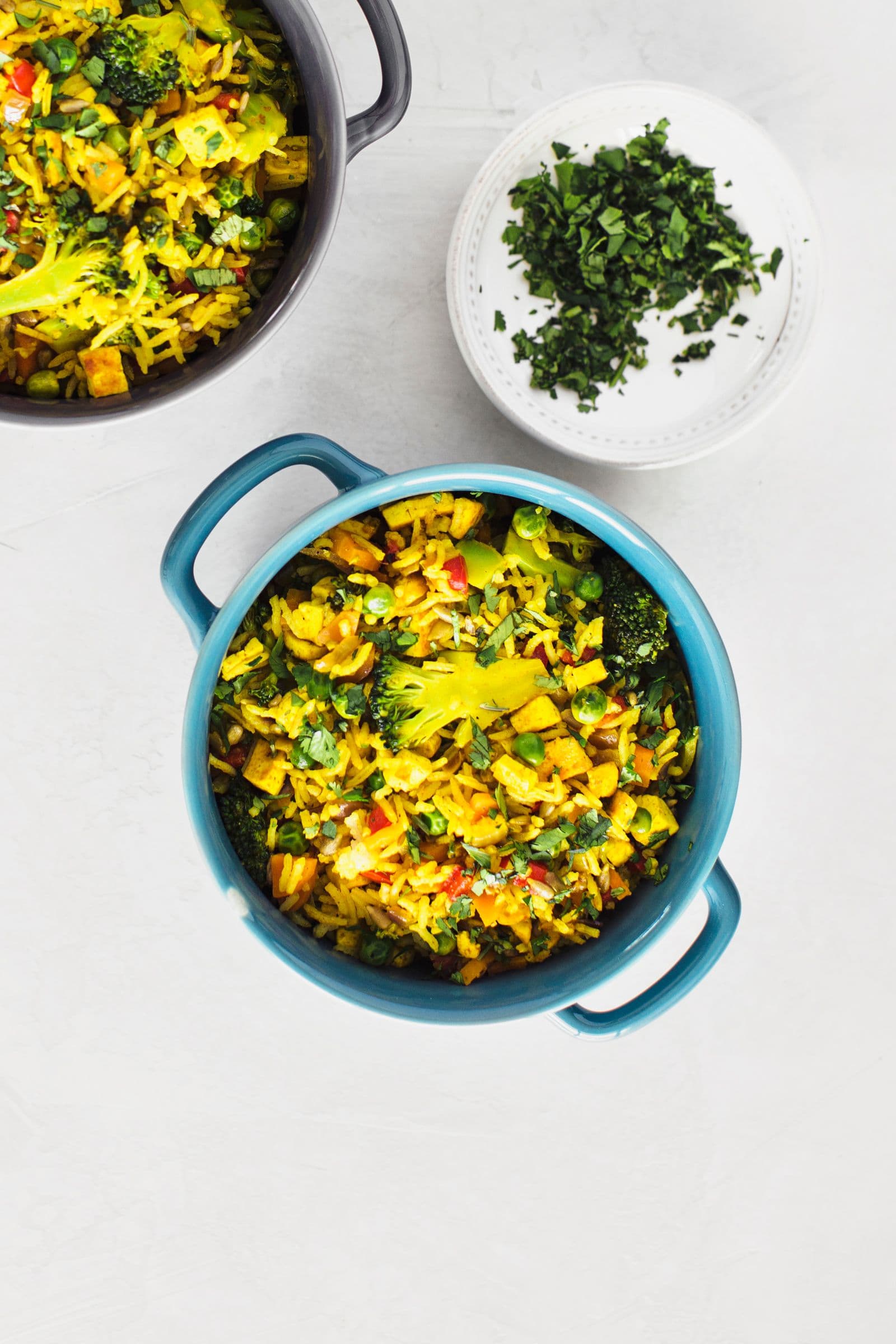 Overhead shot of vegan fried rice in a blue pot with a small bowl of chopped herbs.