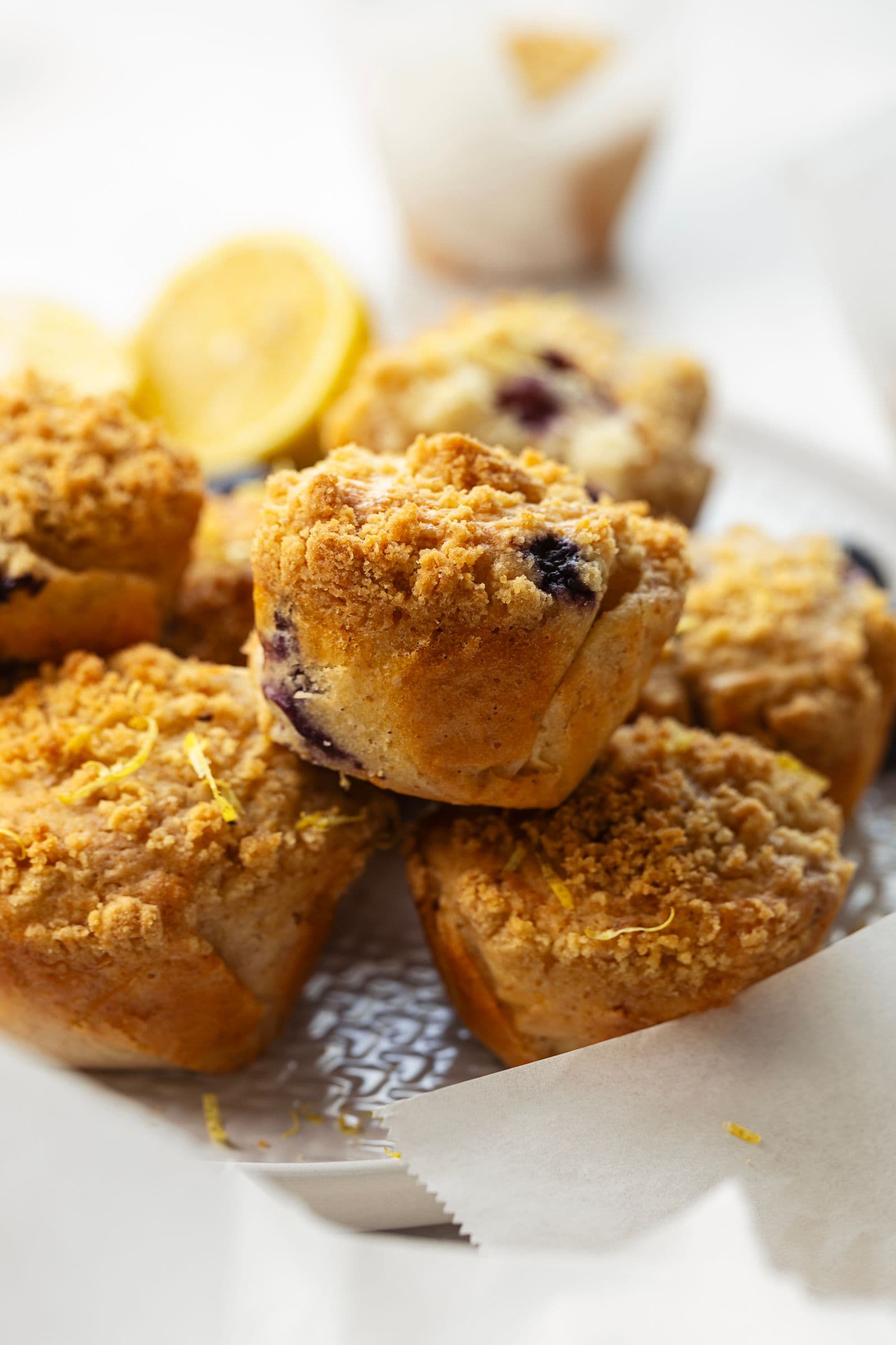 Queques de limão e mirtilos com crumble empilhados num prato, com fundo desfocado.