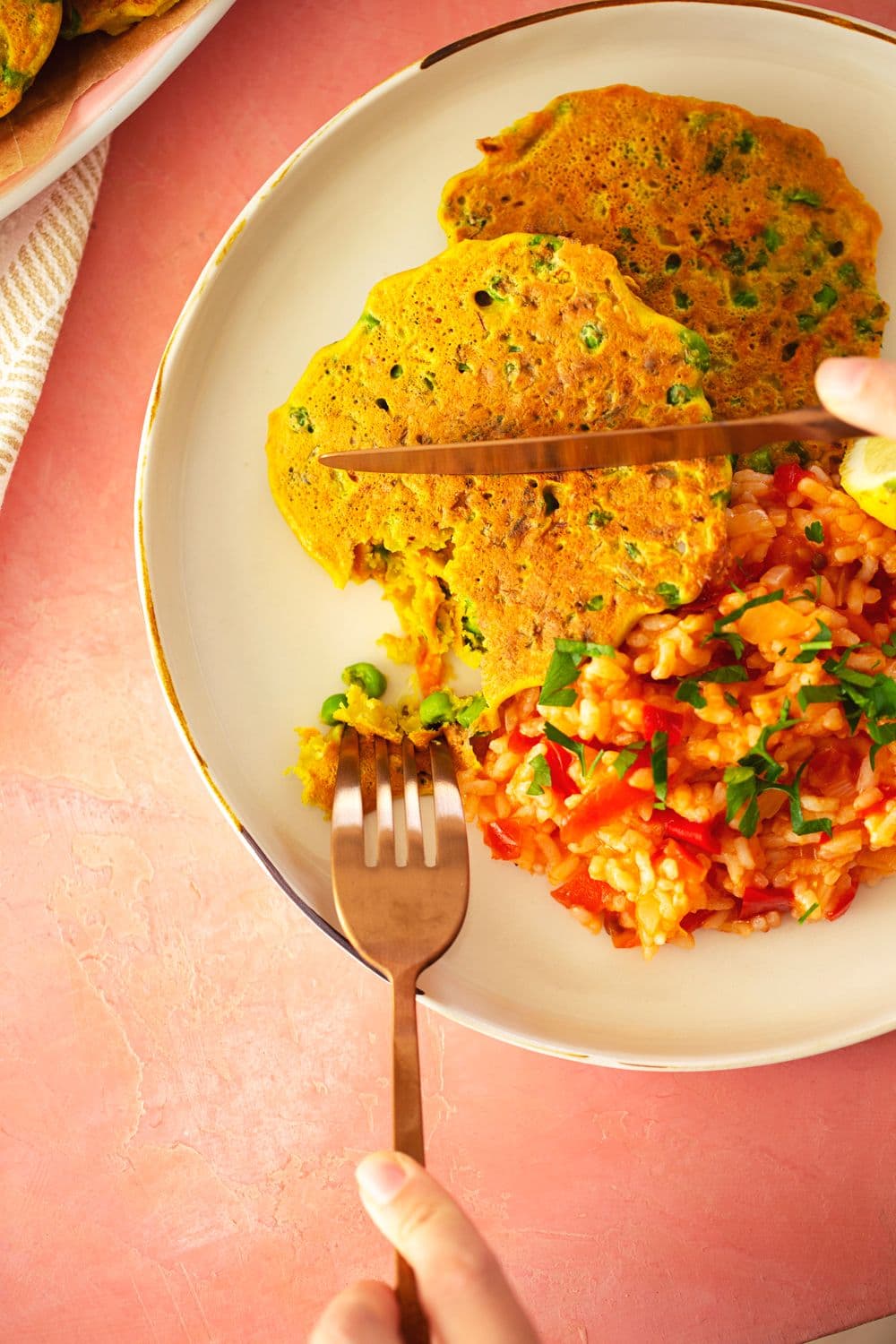 Cutting into a chickpea veggie fritter with a side of saucy tomato rice
