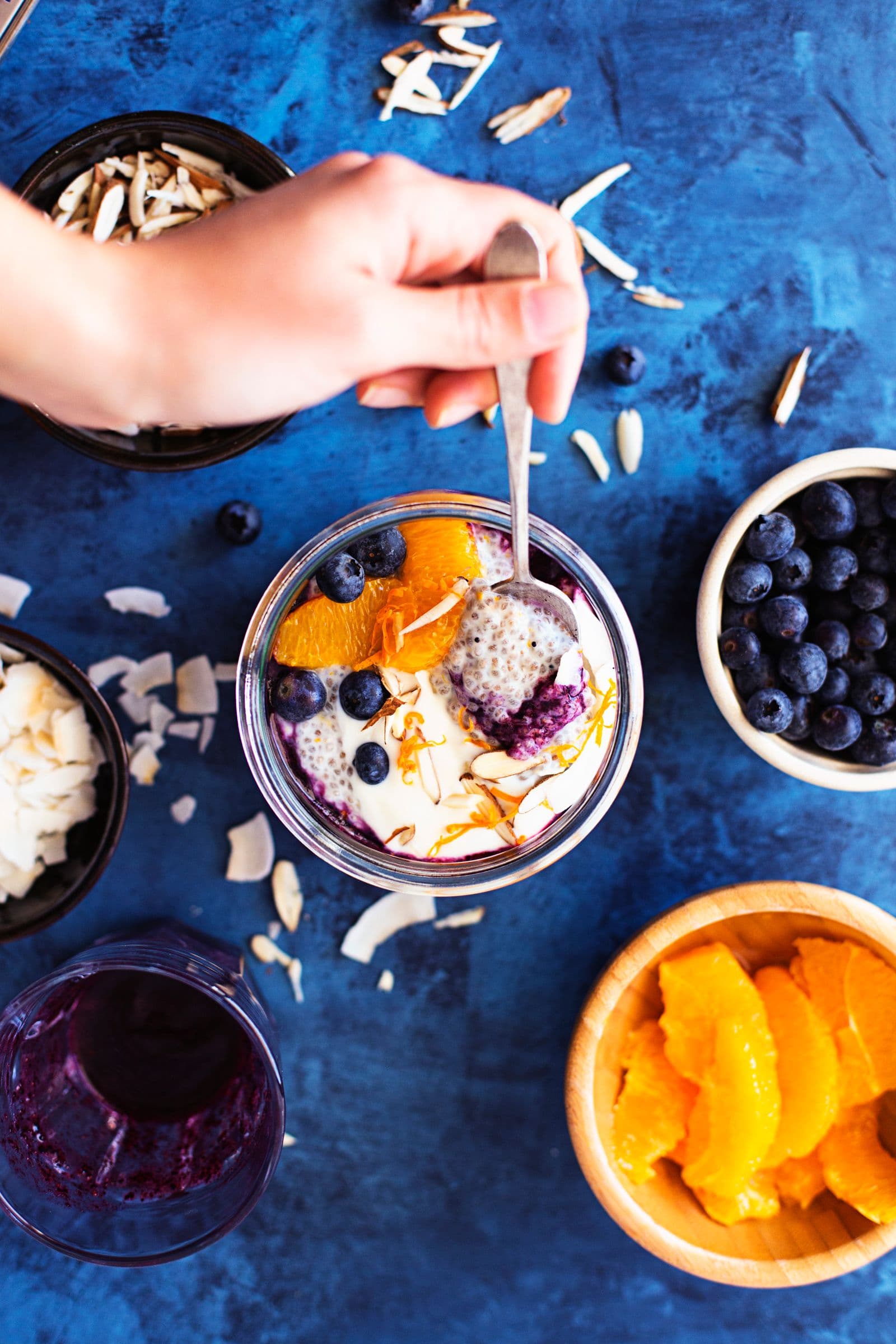 Hand scooping a spoonful of chia pudding with blueberries and almond flakes.