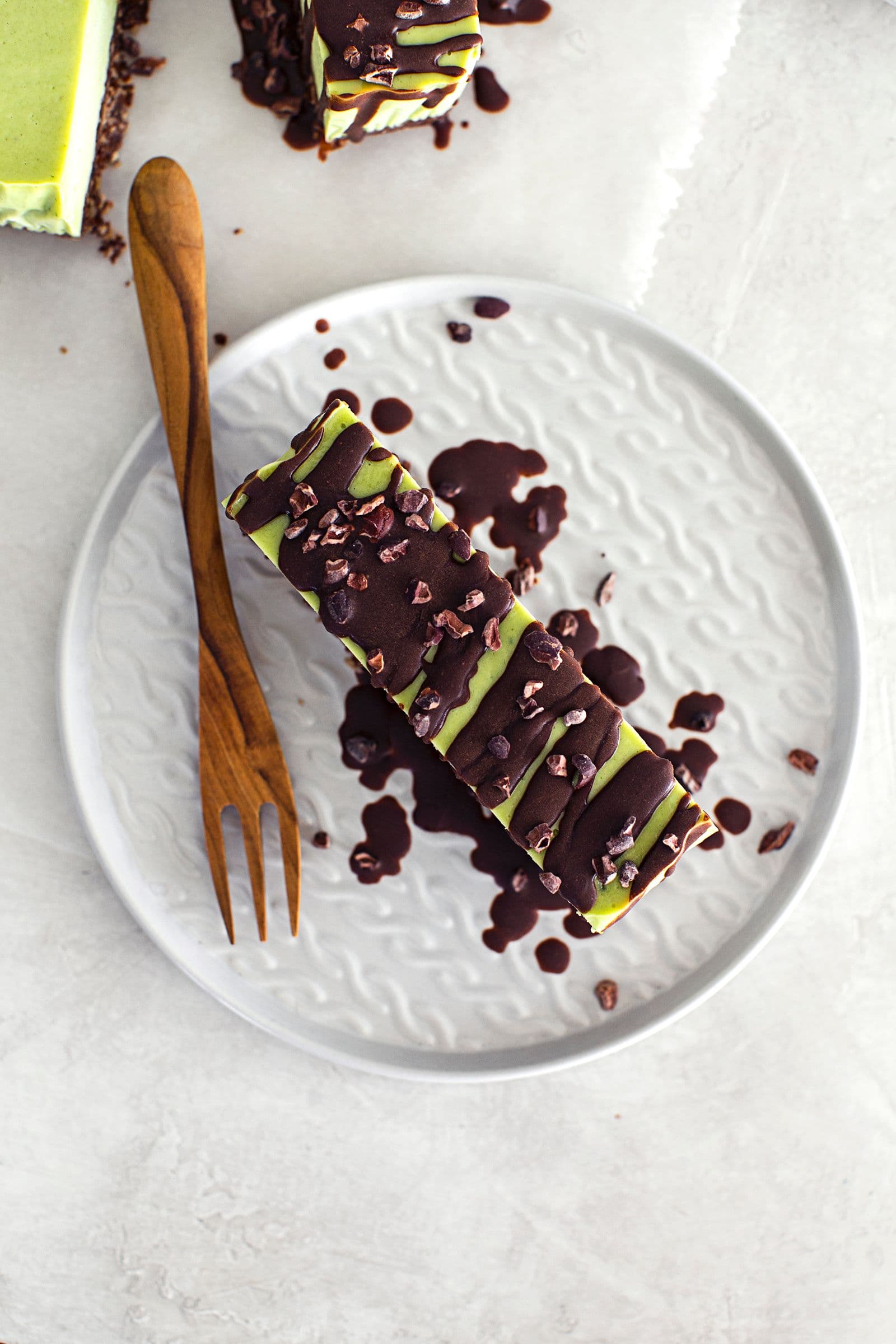 Fatia de cheesecake vegan de menta e chocolate com base de frutos secos, coberta com chocolate derretido e nibs de cacau.