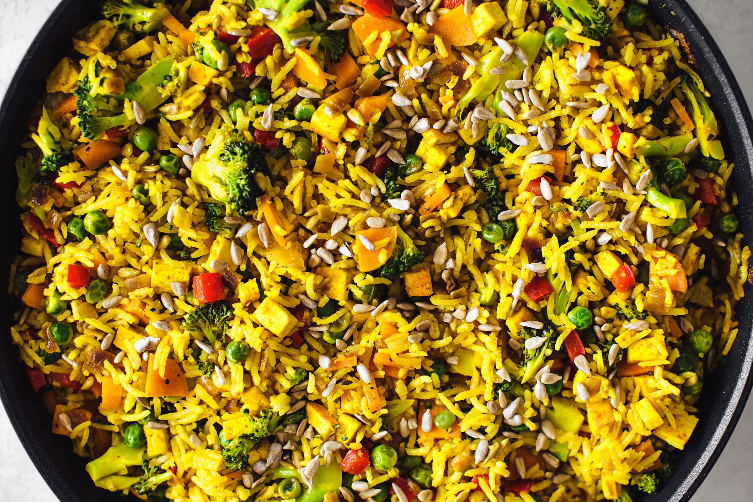 Overhead shot of a full pan of vegan fried rice with sunflower seeds on top.