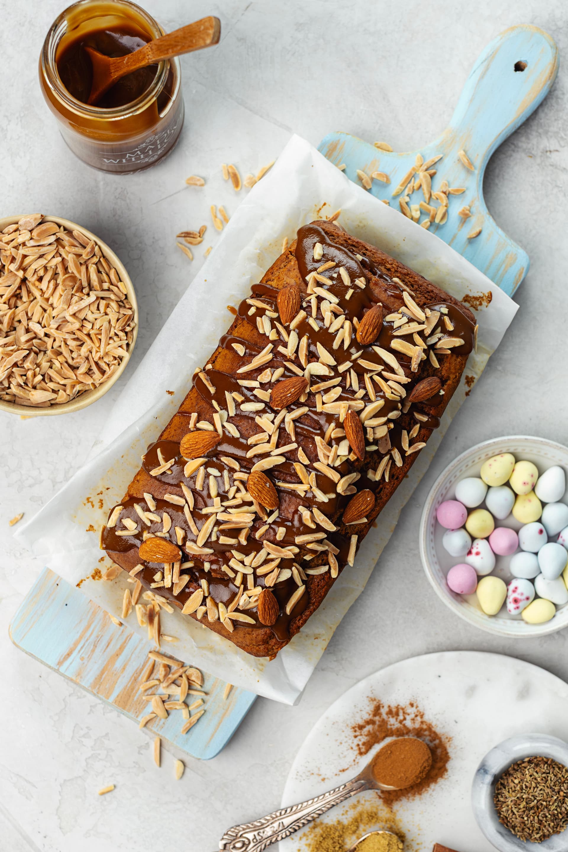 Bolo de amêndoa com caramelo de coco e amêndoas tostadas visto de cima, com ovos de Páscoa e especiarias ao redor.