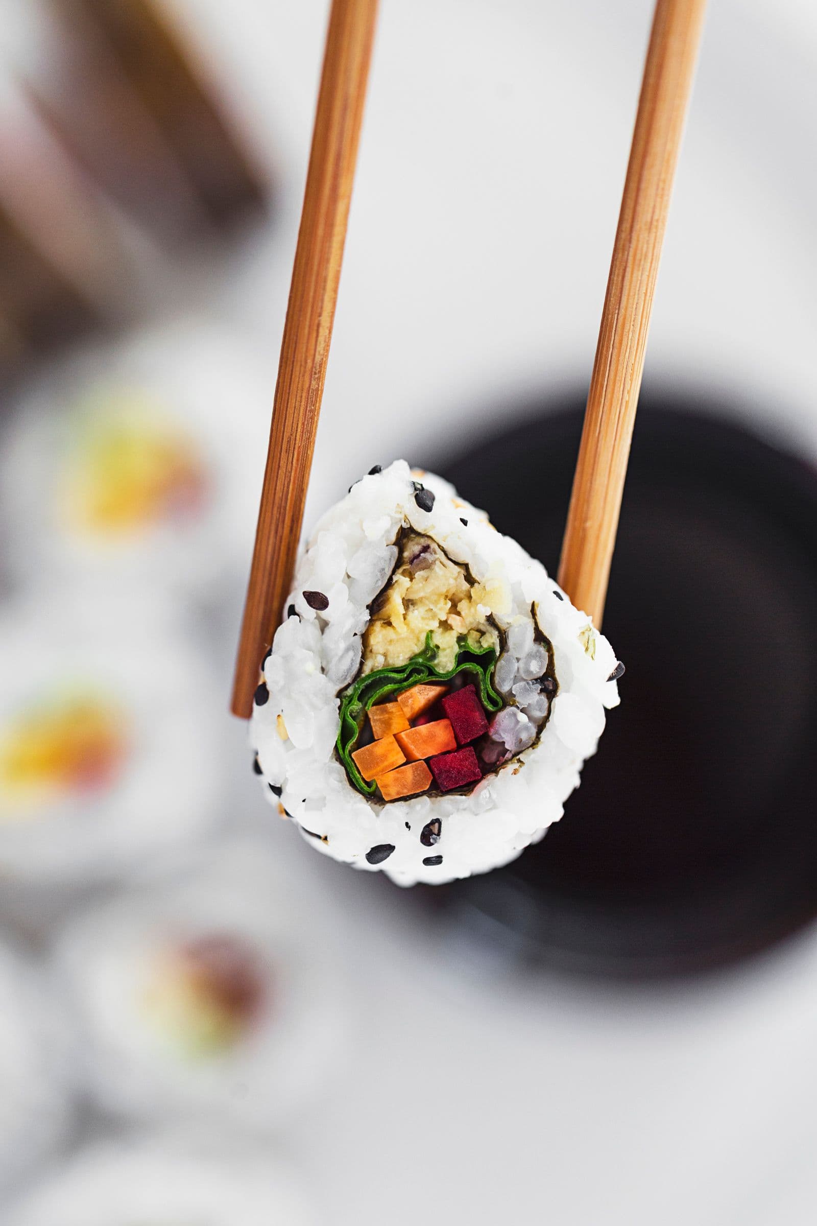 Pauzinhos a segurar um pedaço de sushi vegan no ar.