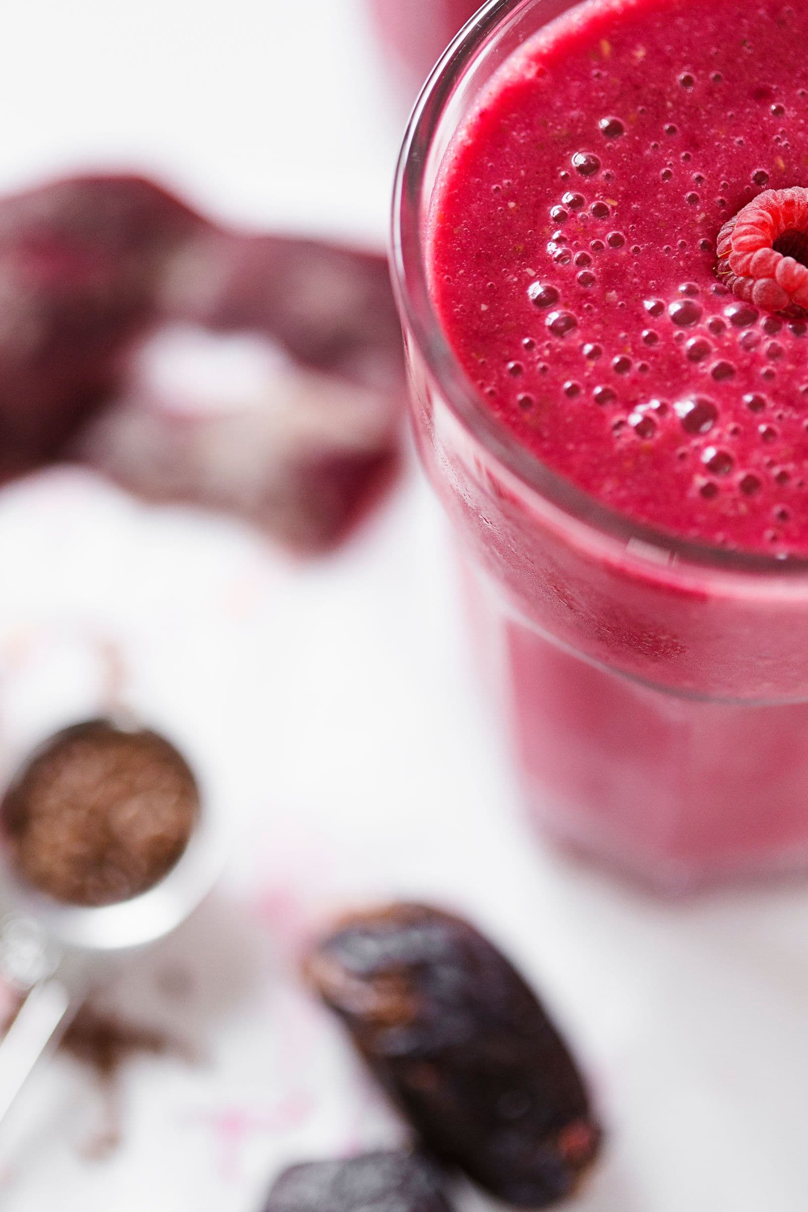 Close-up de um smoothie de beterraba e framboesa num copo com uma framboesa por cima.