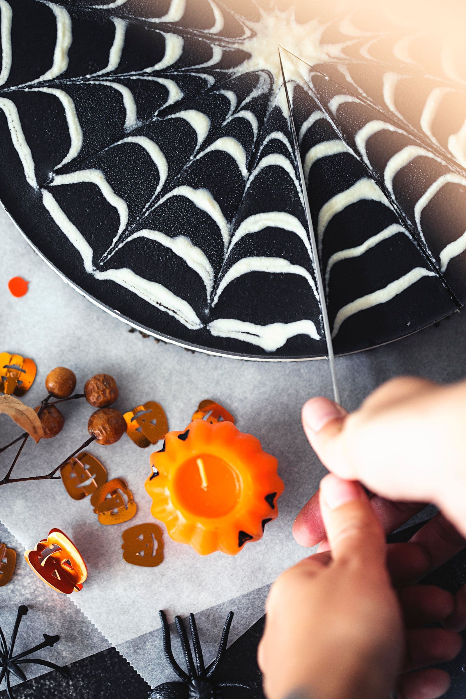 A hand slicing the double chocolate cheesecake decorated with a spiderweb pattern.
