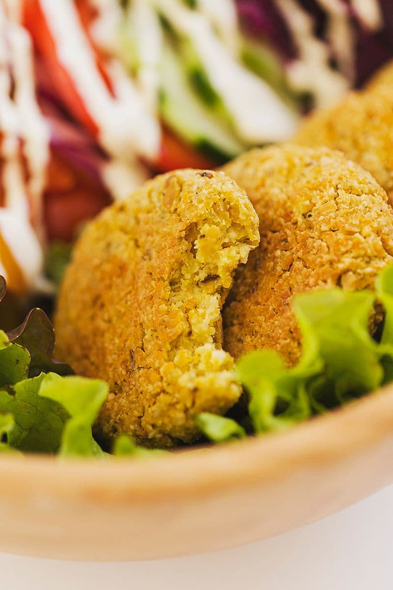Close-up of bitten falafel in salad bowl with veggies.