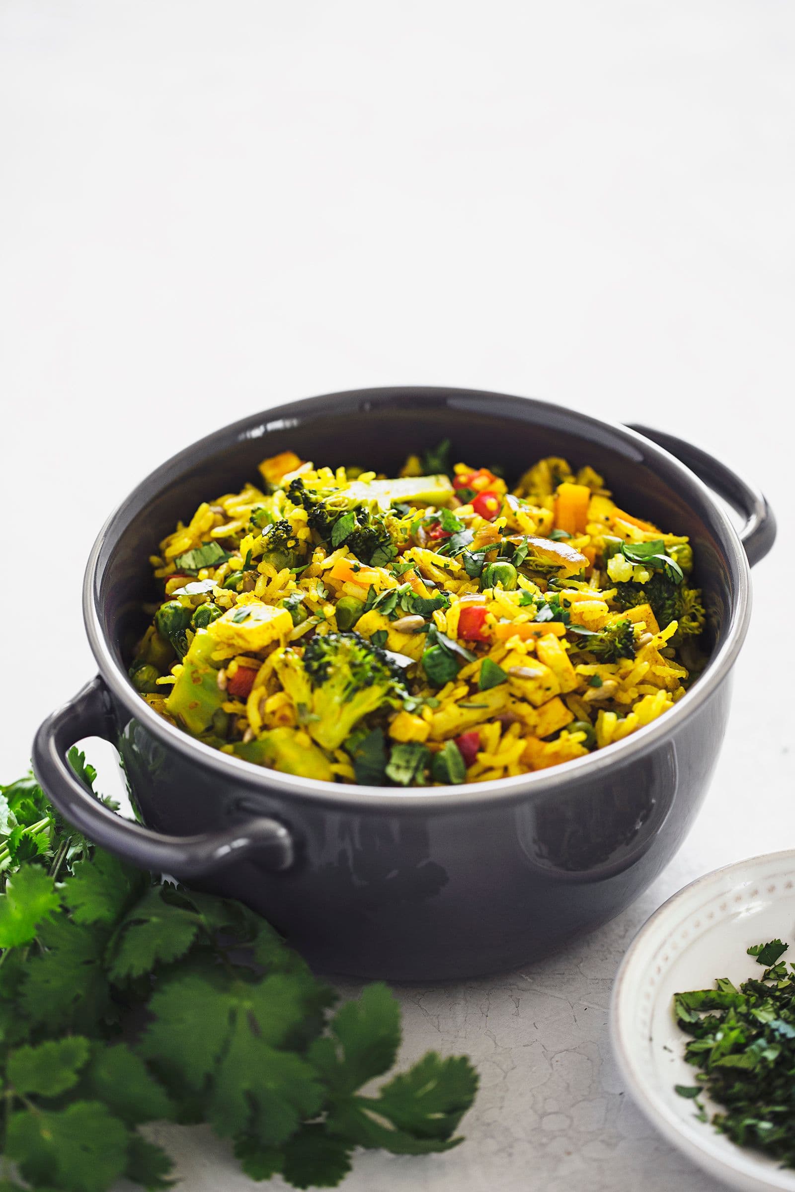 Cerâmica individual com arroz frito vegan ao lado de coentros frescos numa taça.