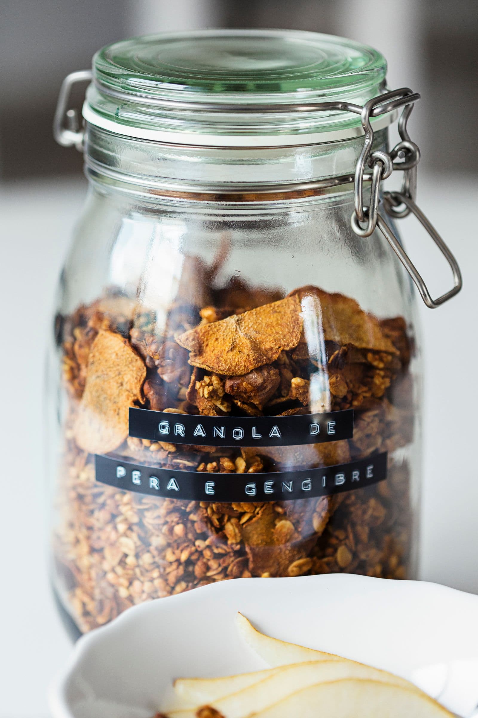 Close-up de um frasco de vidro com granola rotulado “Granola de Pêra e Gengibre.”