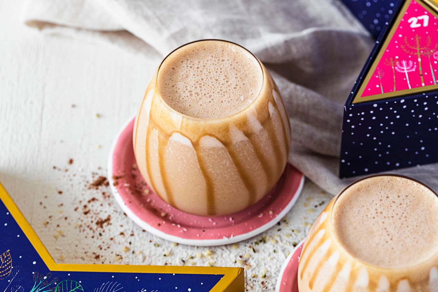 Rounded glass with salted caramel and peanut butter smoothie, drizzled with caramel sauce, on a pink coaster.