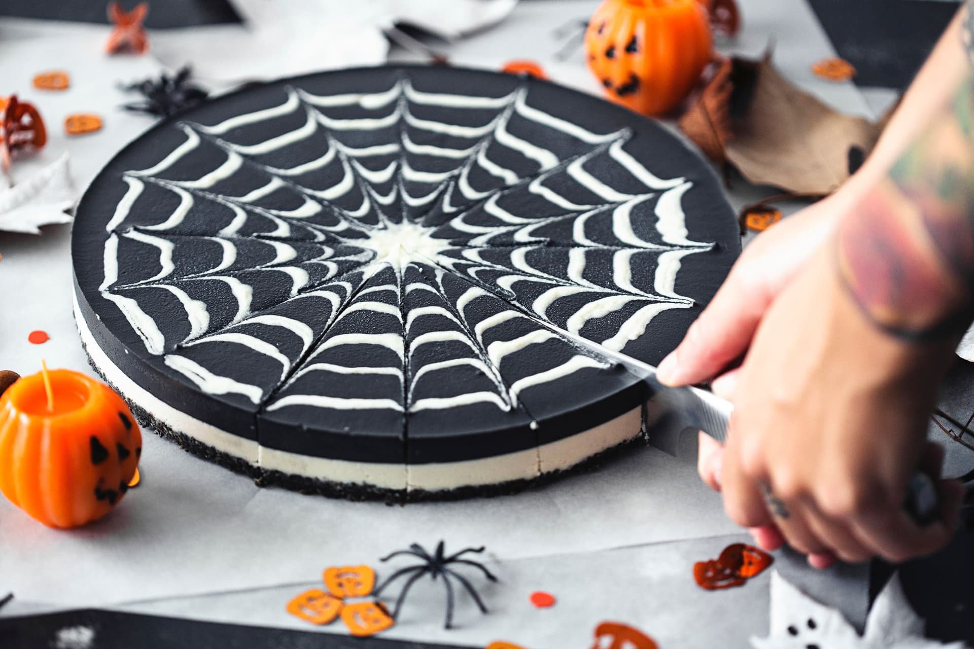 A hand slicing the double chocolate cheesecake decorated with a spiderweb pattern.