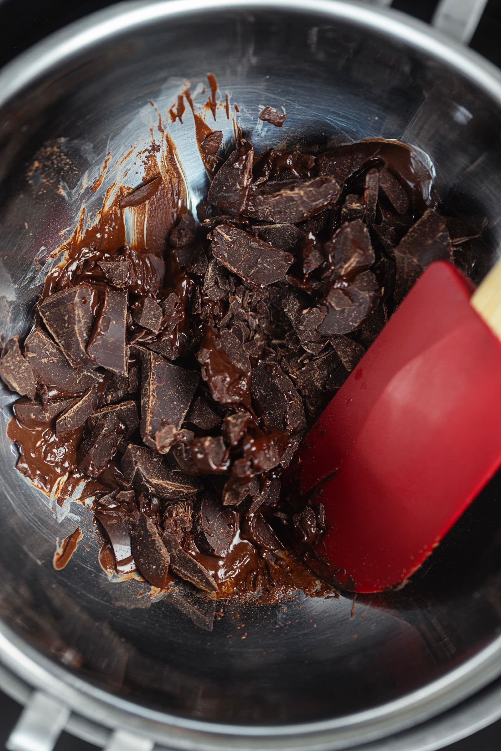 Chocolate negro picado a derreter em banho-maria numa taça de inox, com espátula de silicone.