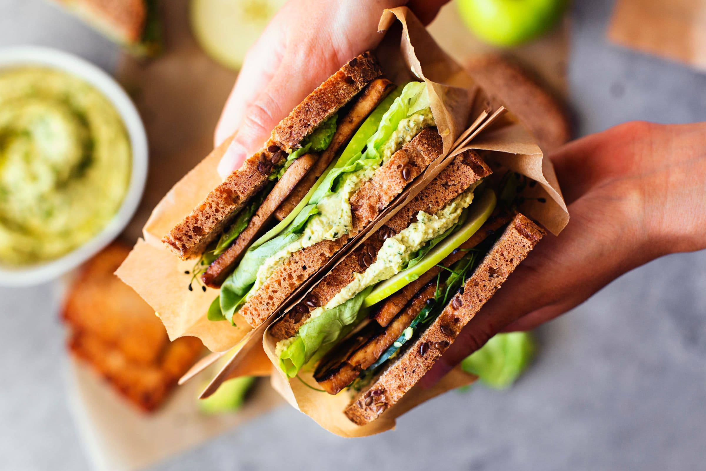 Hands holding assembled sandwiches mid-air.