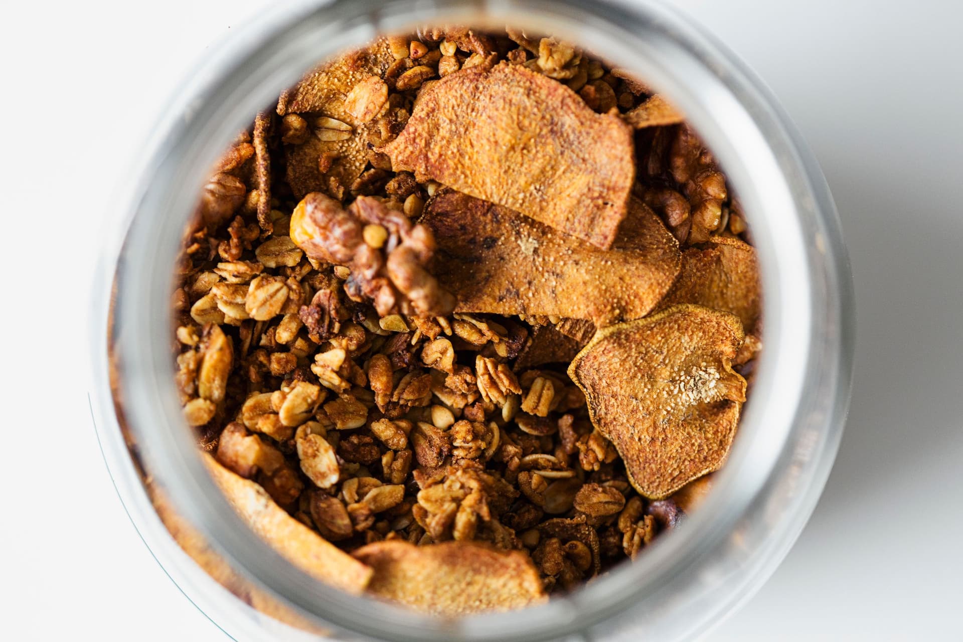Frasco de granola dourada com fatias de pêra desidratada visto de cima.