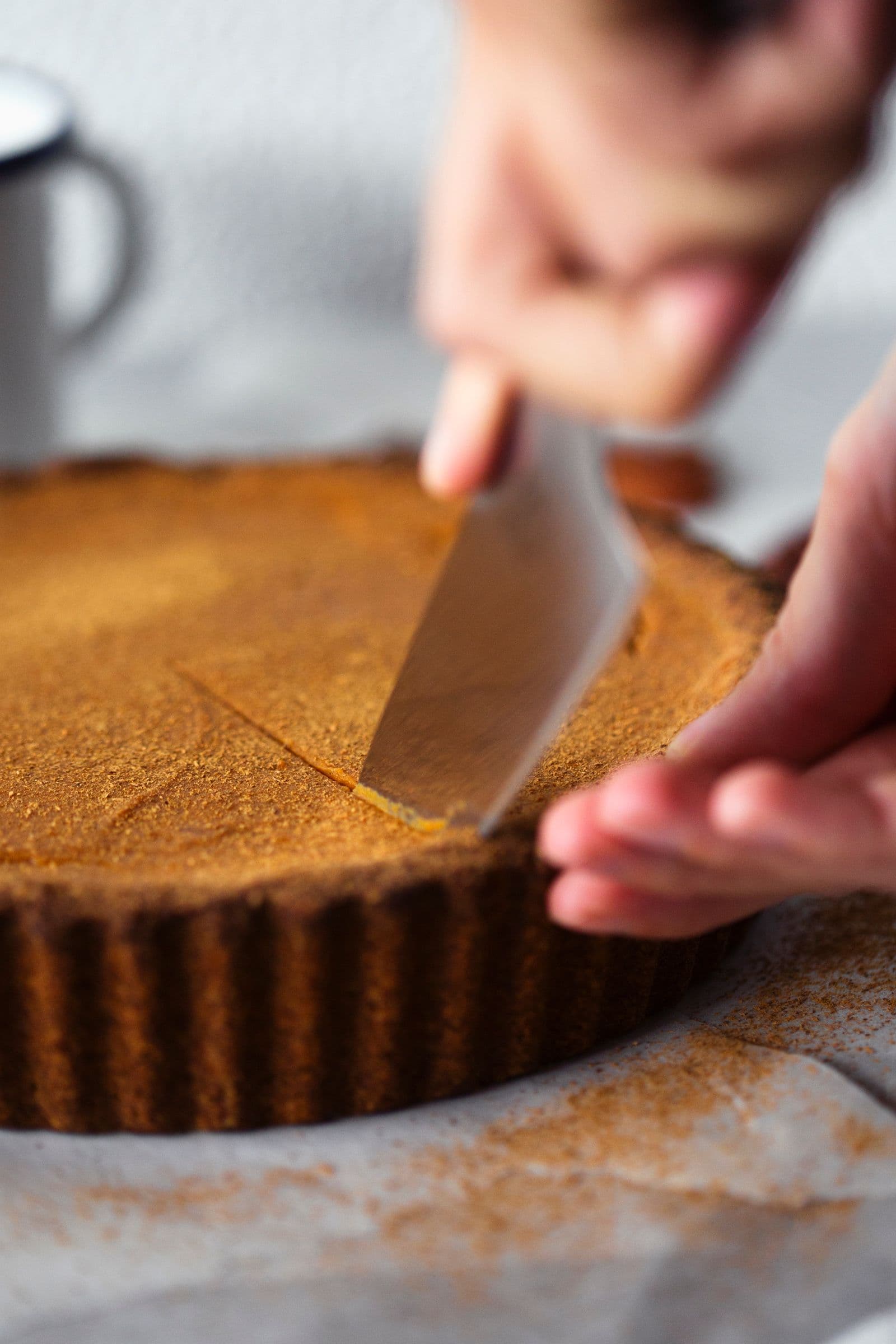 Close-up of a knife slicing into the freshly baked and chilled sweet potato pie crust.