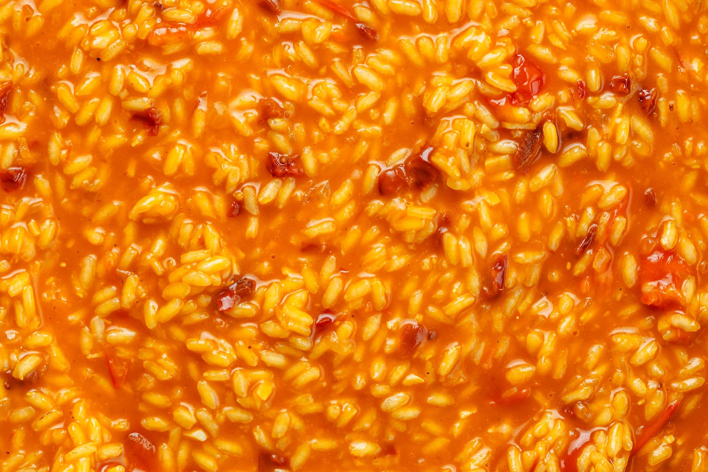 Close-up do risotto de tomate cremoso, com grãos de arroz brilhantes envolvidos num molho vermelho intenso.