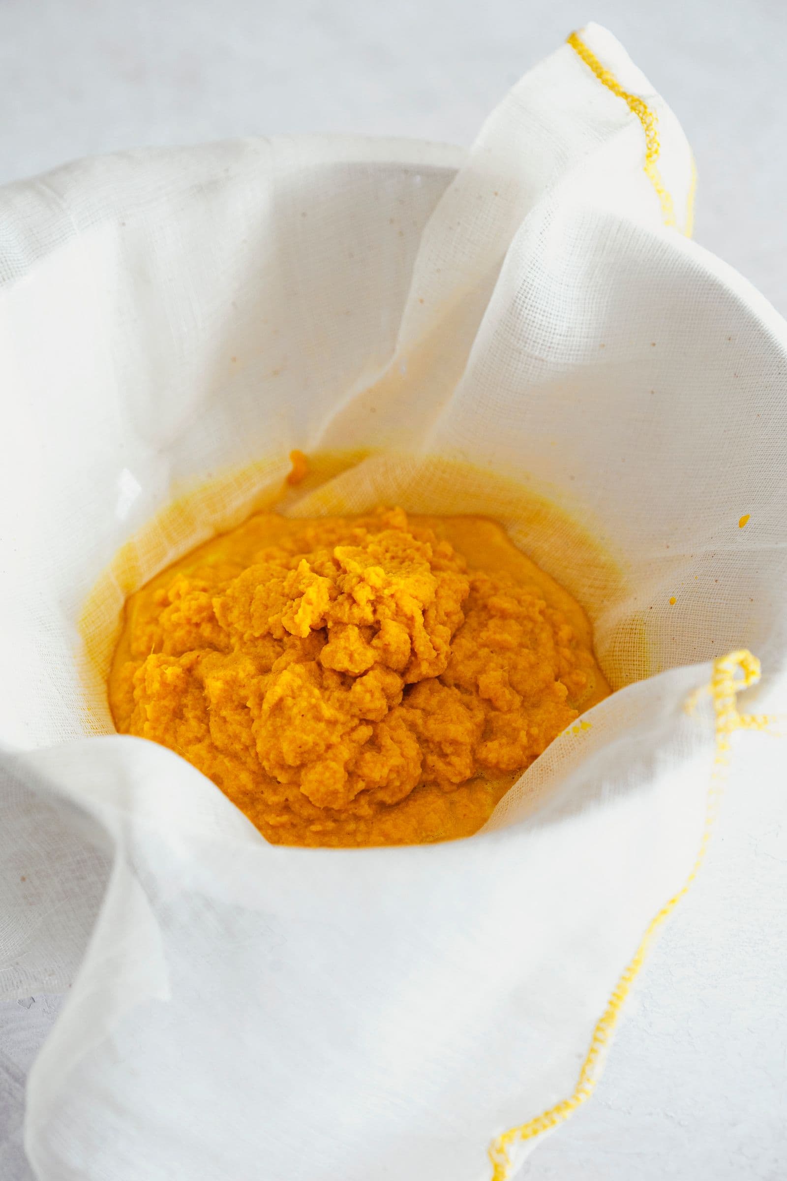 Pano de cozinha a coar a polpa de gengibre e curcuma antes de espremer.