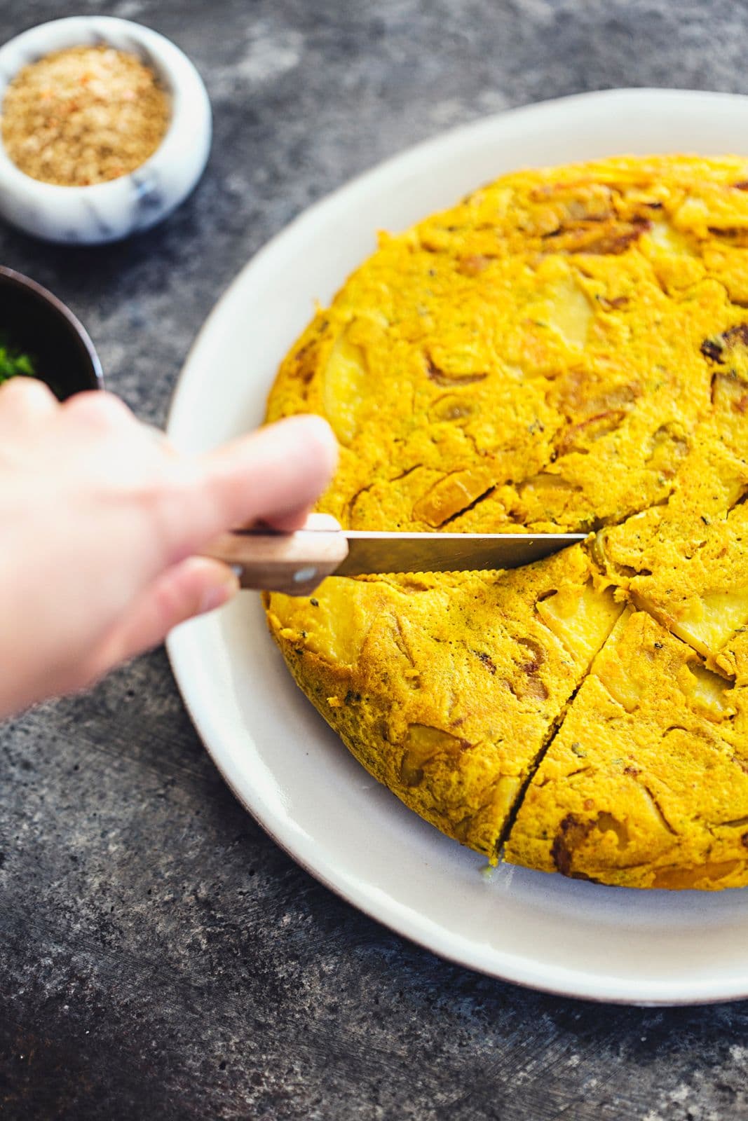 Mão a usar uma faca para cortar a tortilha num prato branco.