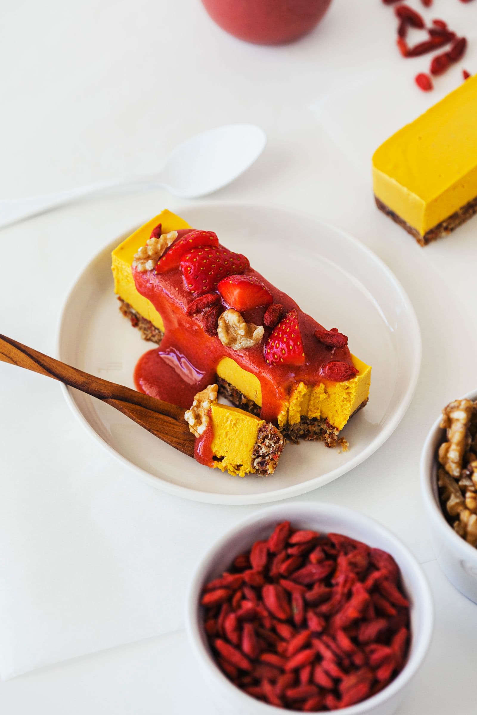 Wooden fork taking a bite of raw vegan cheesecake with fruity topping.