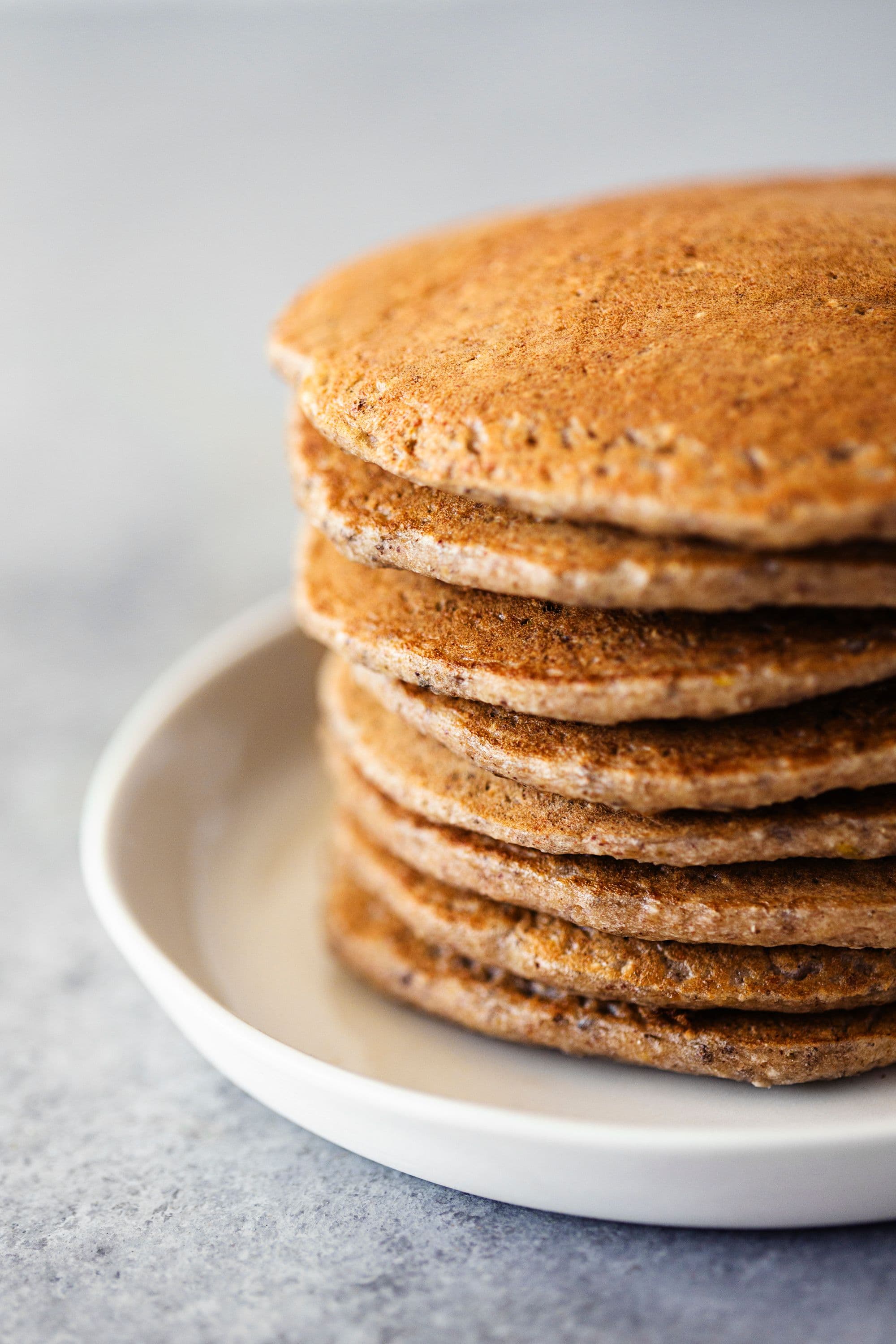 Tall stack of fluffy oatmeal pancakes on a white plate.