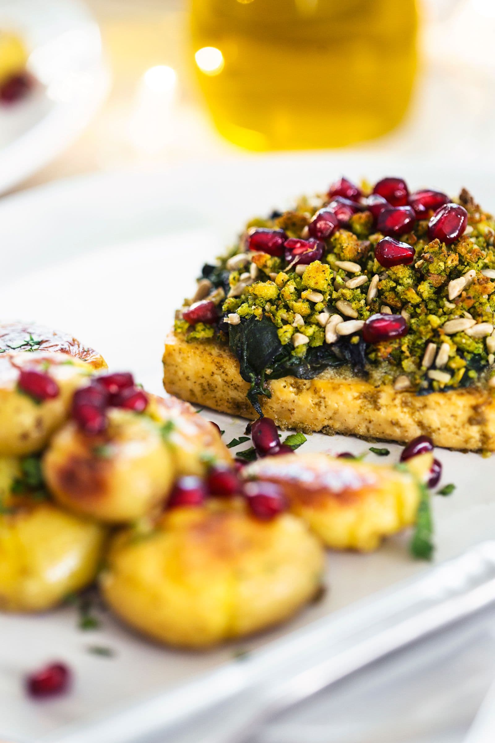 Close-up side view of tofu roast slice with golden crust, cornbread crumble and pomegranate seeds.