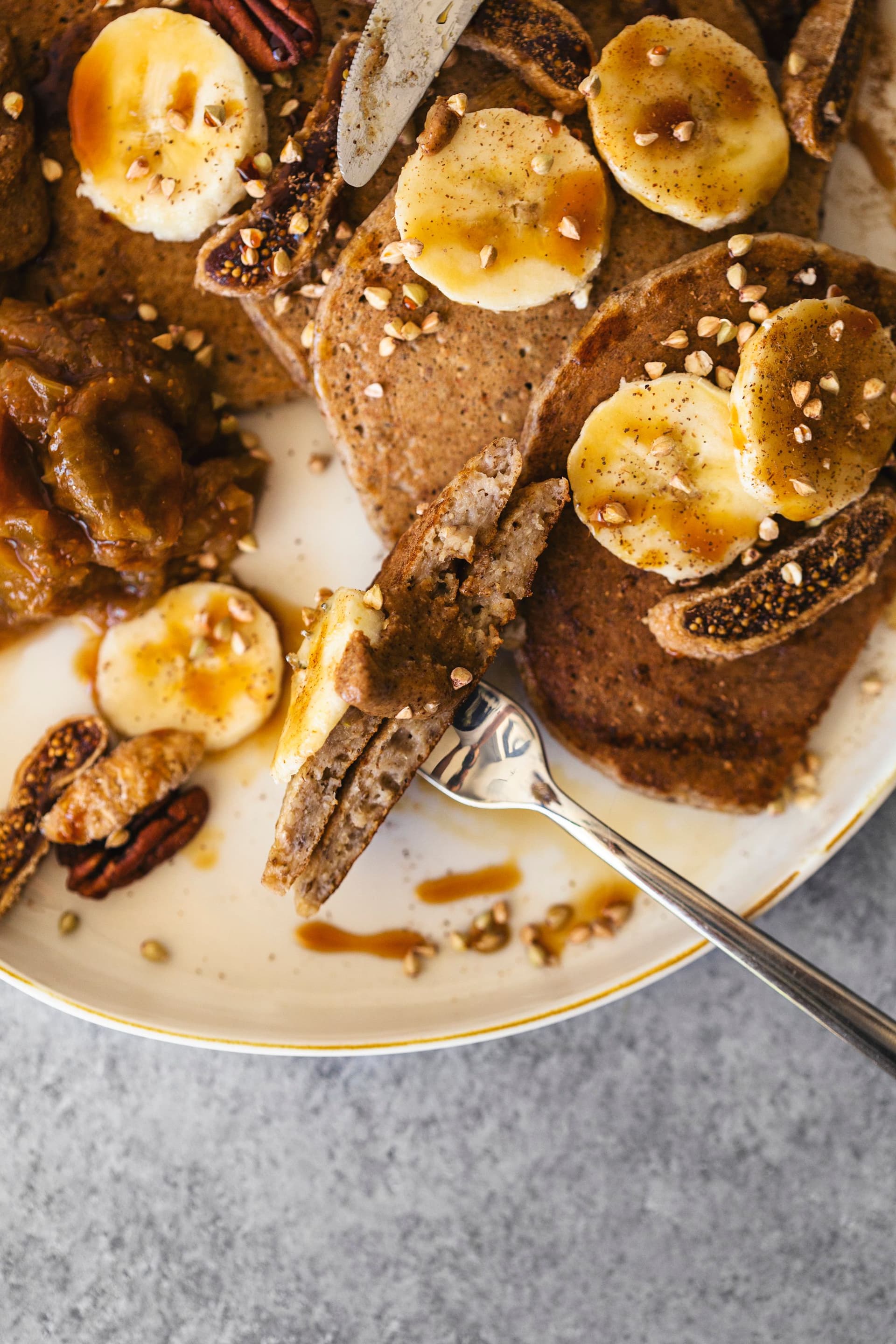 Close-up de garfo a cortar panquecas com cobertura de banana e manteiga de frutos secos.