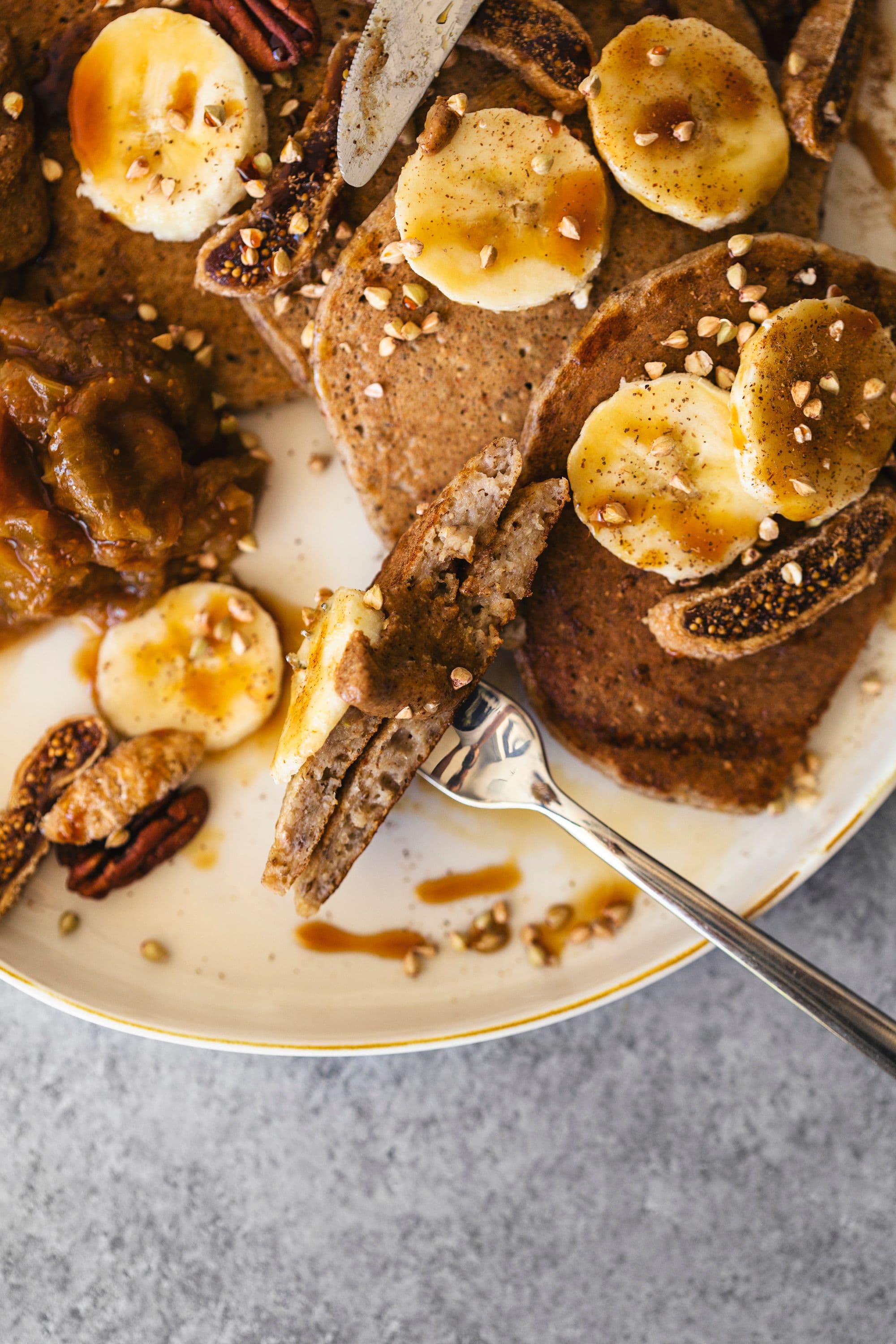 Close-up of a fork cutting through a stack of pancakes topped with banana and nut butter.