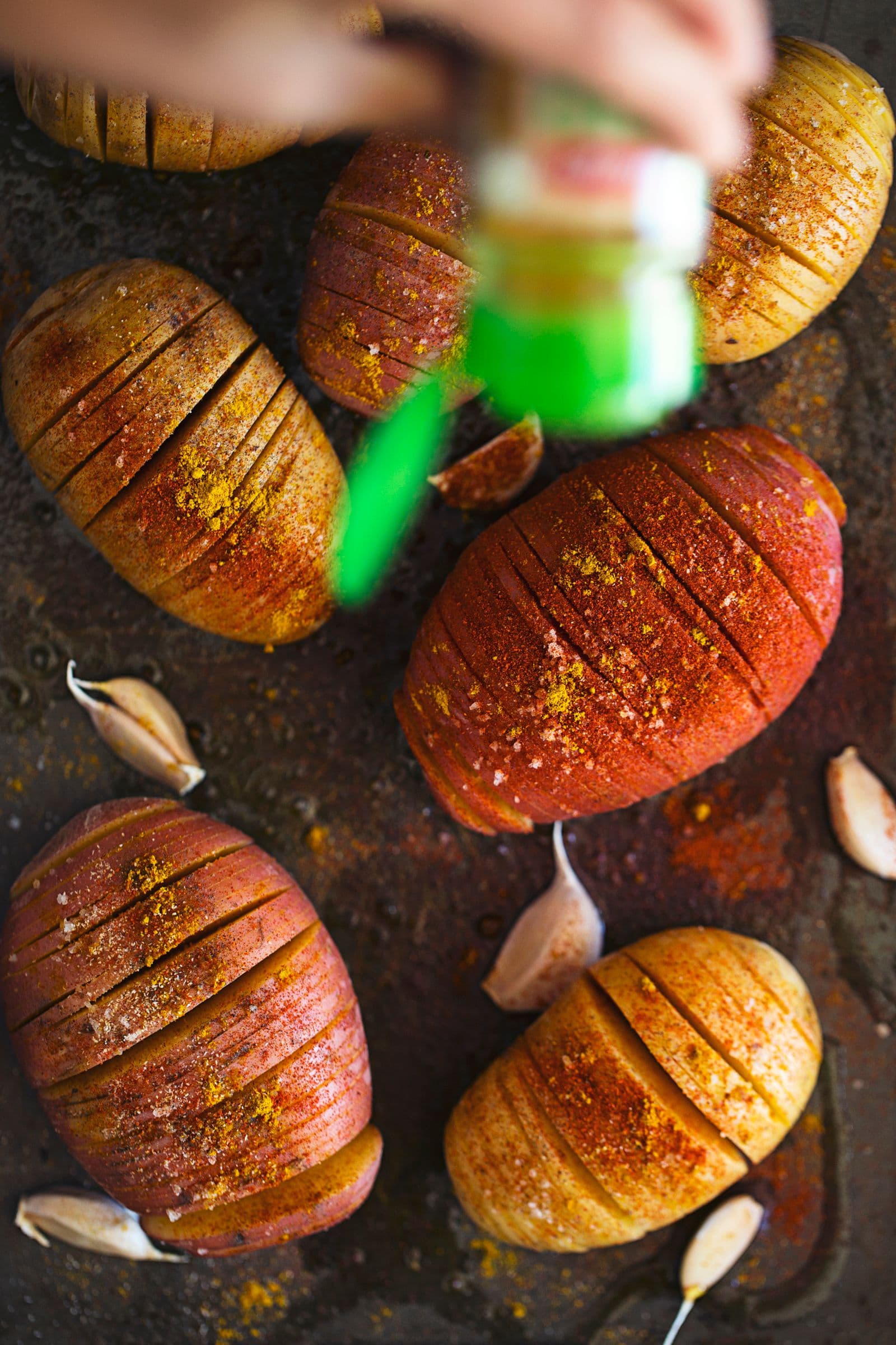 Seasoning Hasselback potatoes on a baking sheet with vibrant spices and garlic.