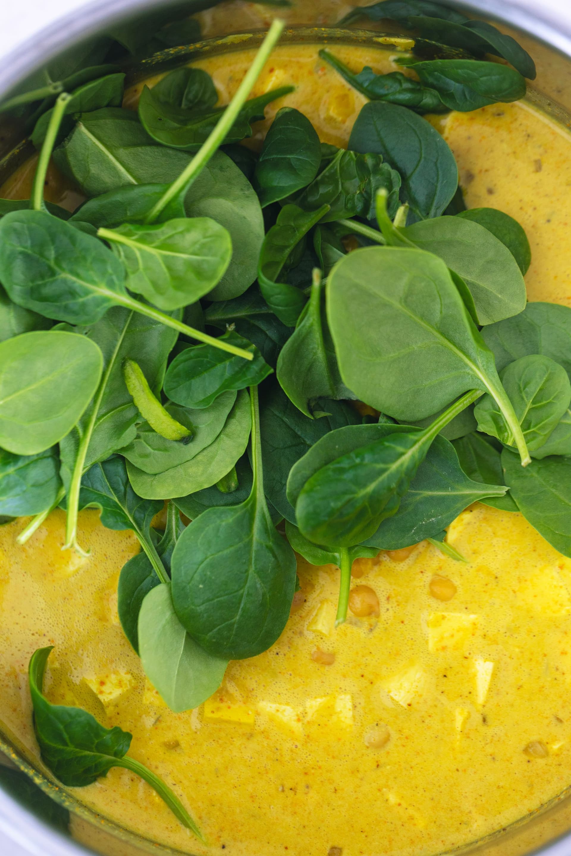 Fresh spinach leaves being added to a creamy yellow curry base.