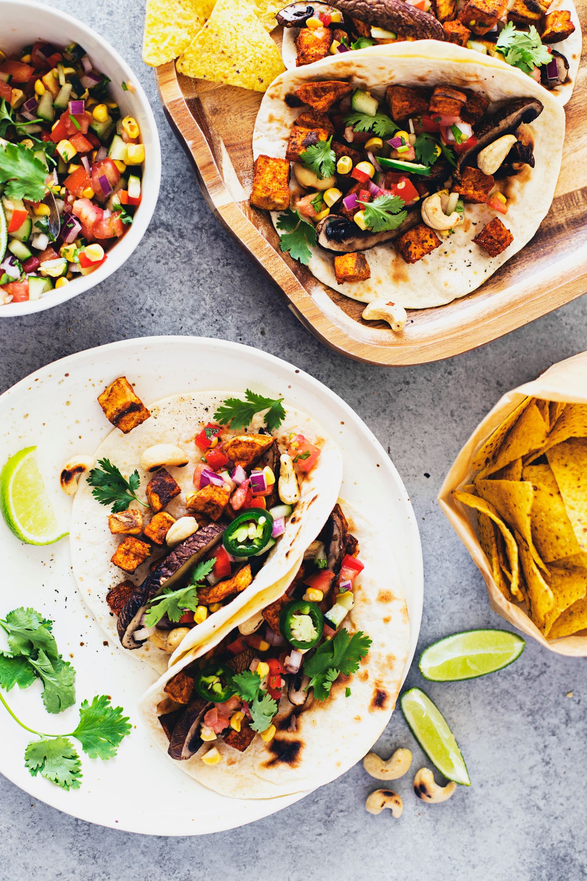 Pratos com dois tacos cada, molho, nachos e gomos de lima.