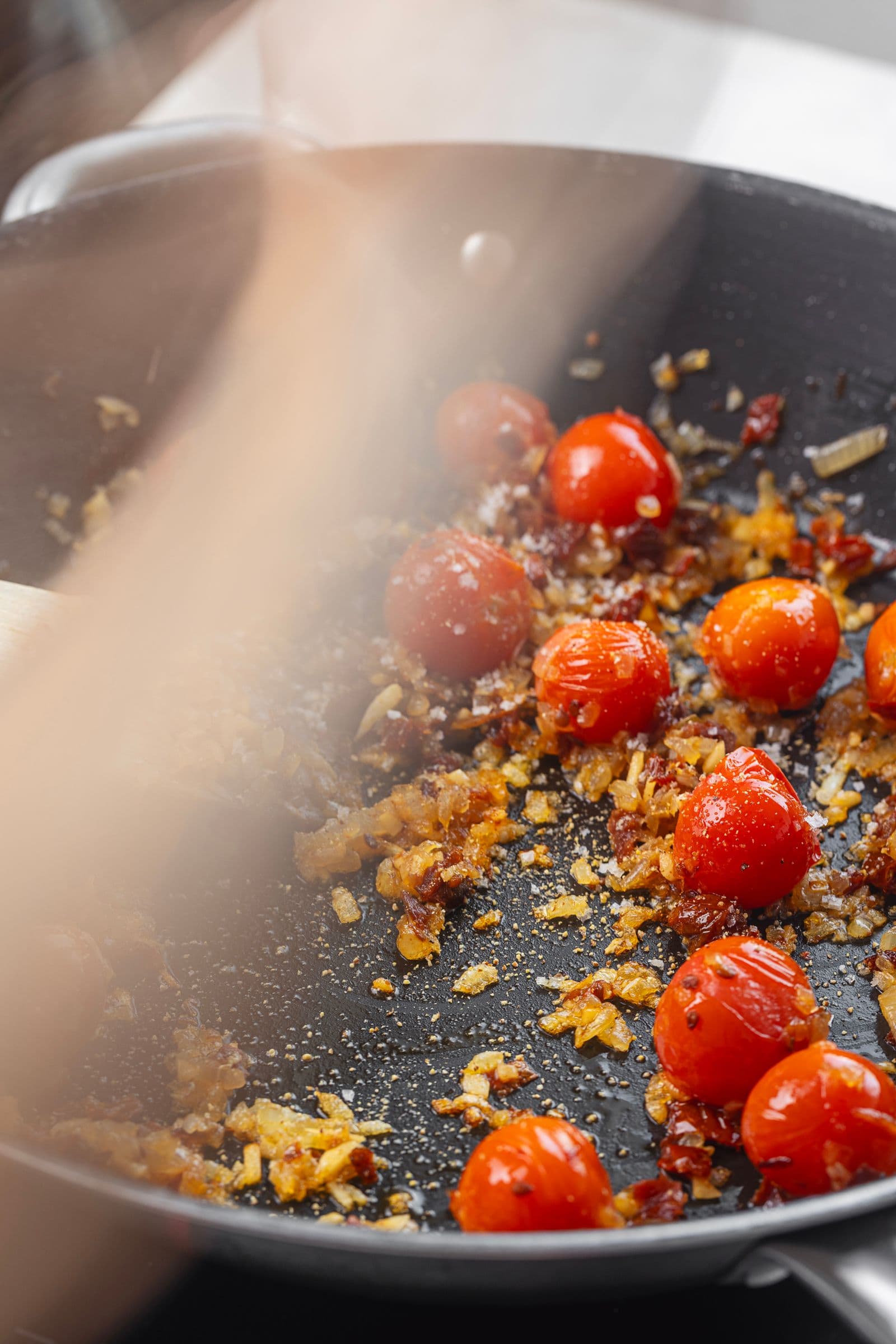 Frigideira com vapor, onde tomates-cereja e cebola dourada cozinham para a base do risotto.