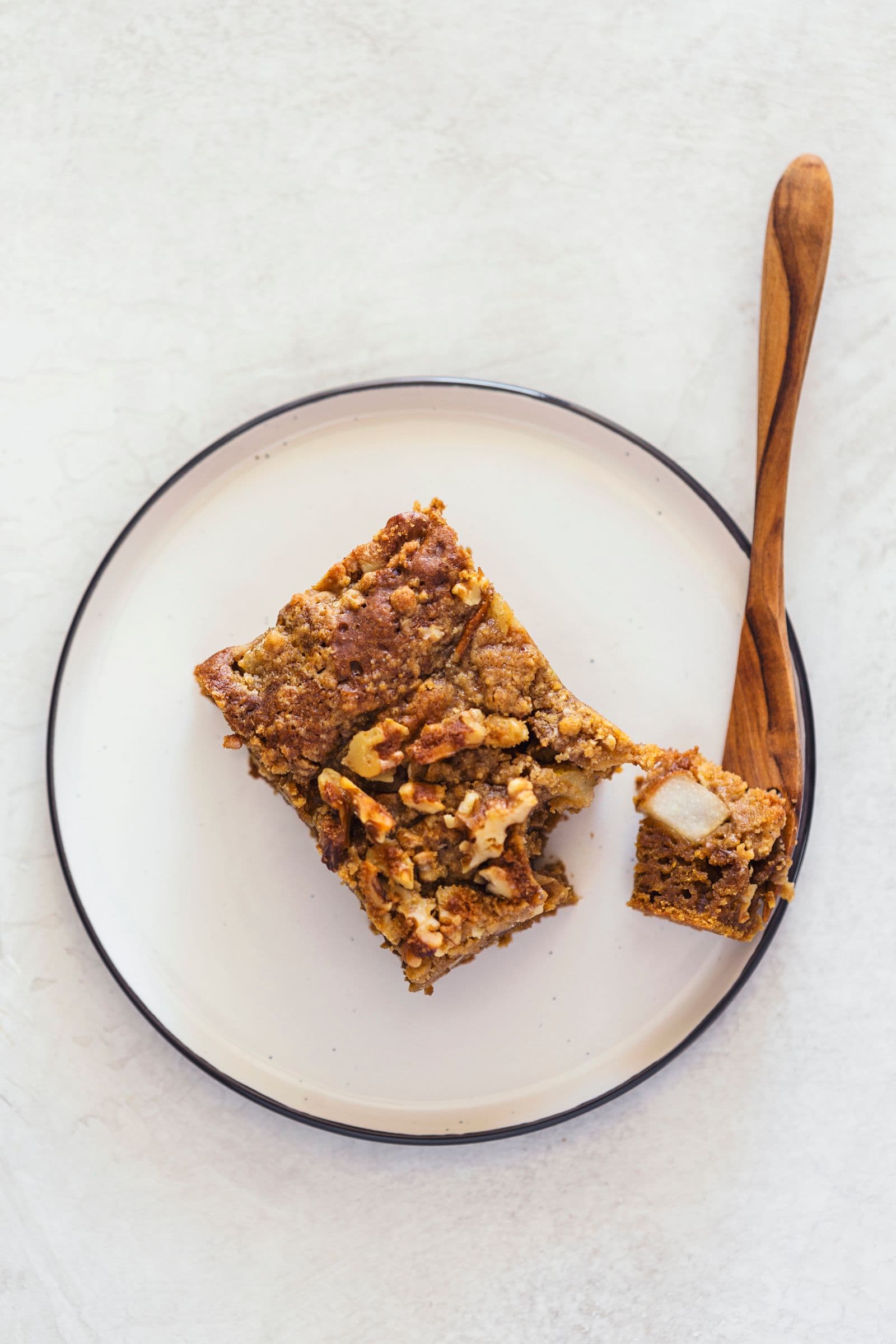 A bite taken out of a slice of coffee cake, resting on a plate with a wooden fork.