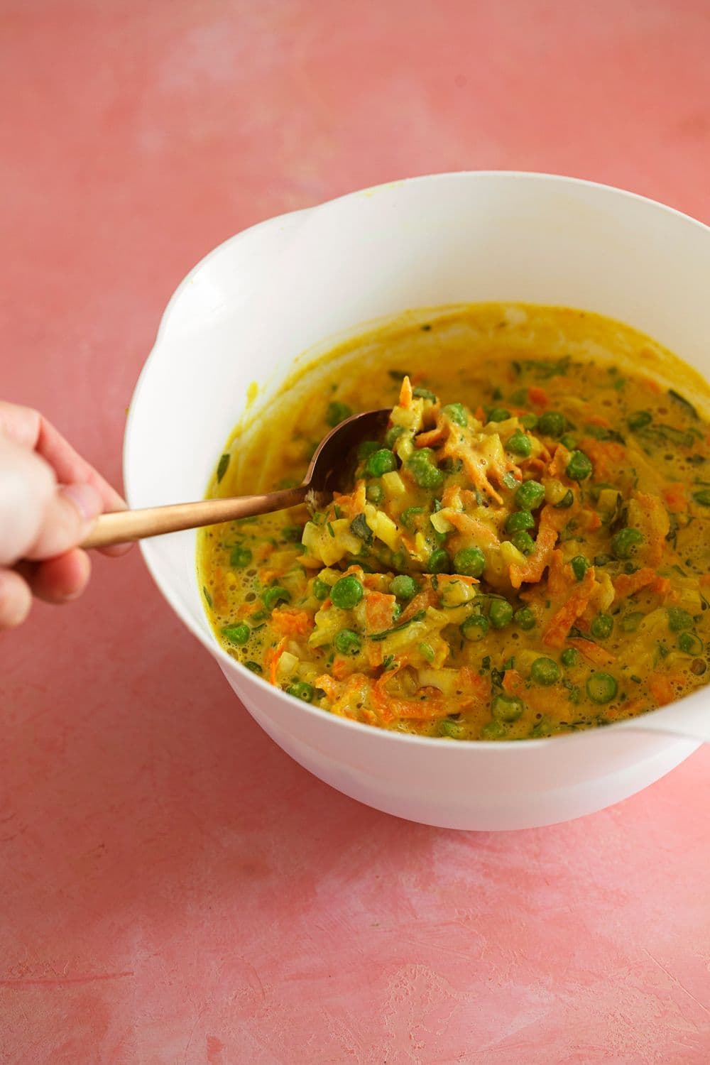 Massa de pataniscas de legumes com farinha de grão, cenoura ralada e ervilhas, numa taça branca