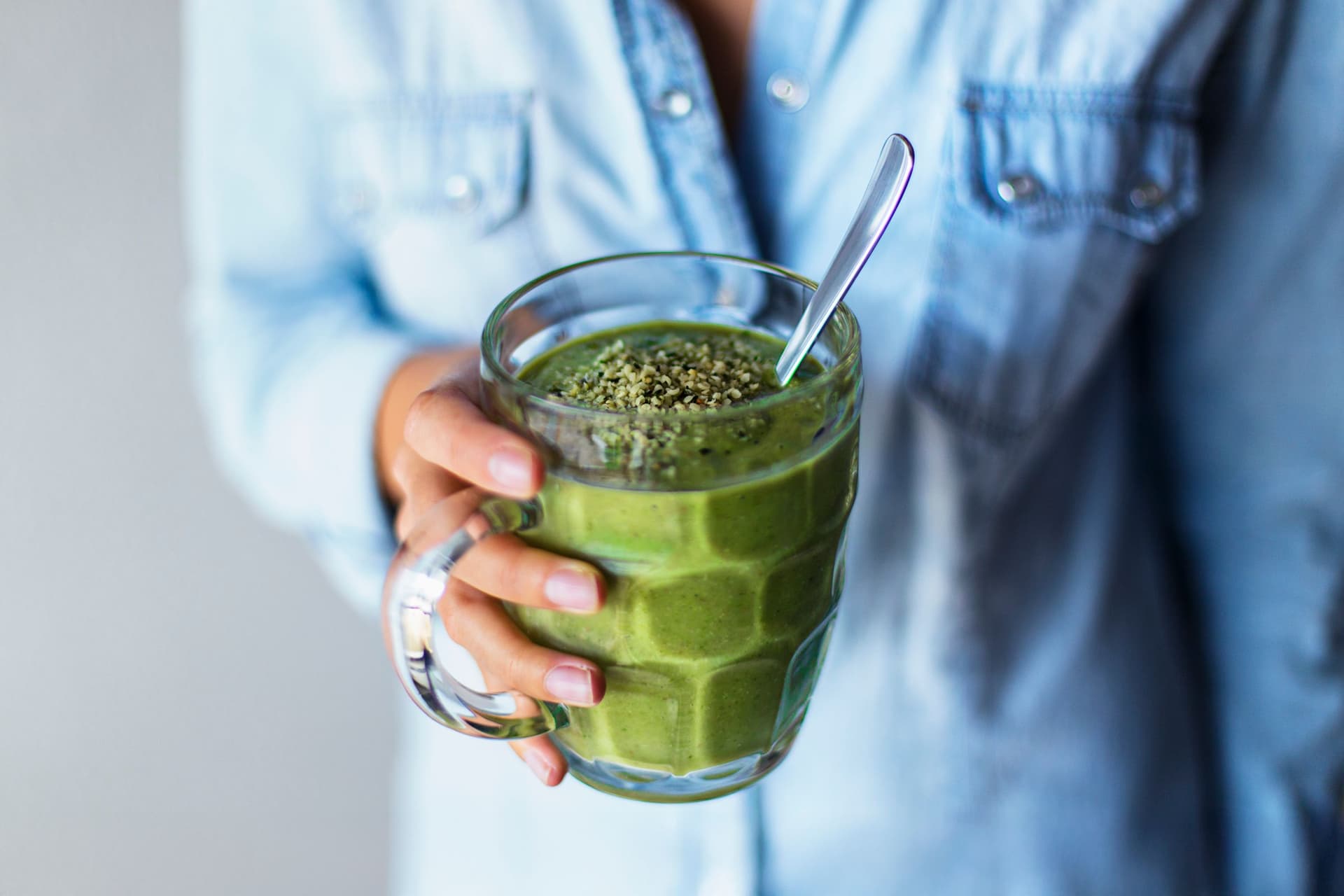 Person holding a glass of green smoothie with a metal straw.