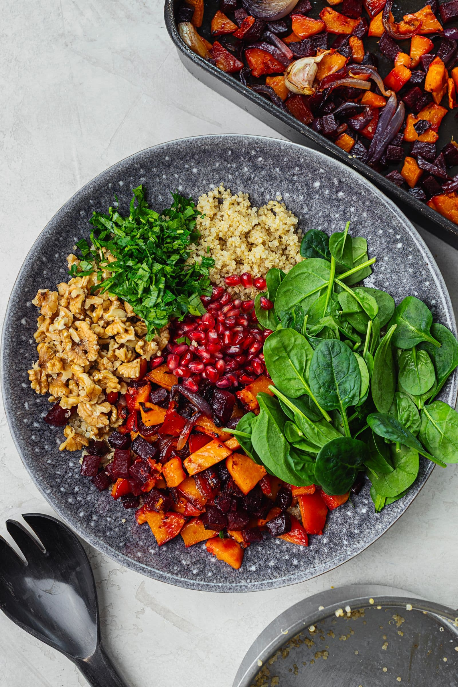 Winter salad in preparation with quinoa, roasted vegetables, spinach, walnuts, pomegranate and fresh herbs.