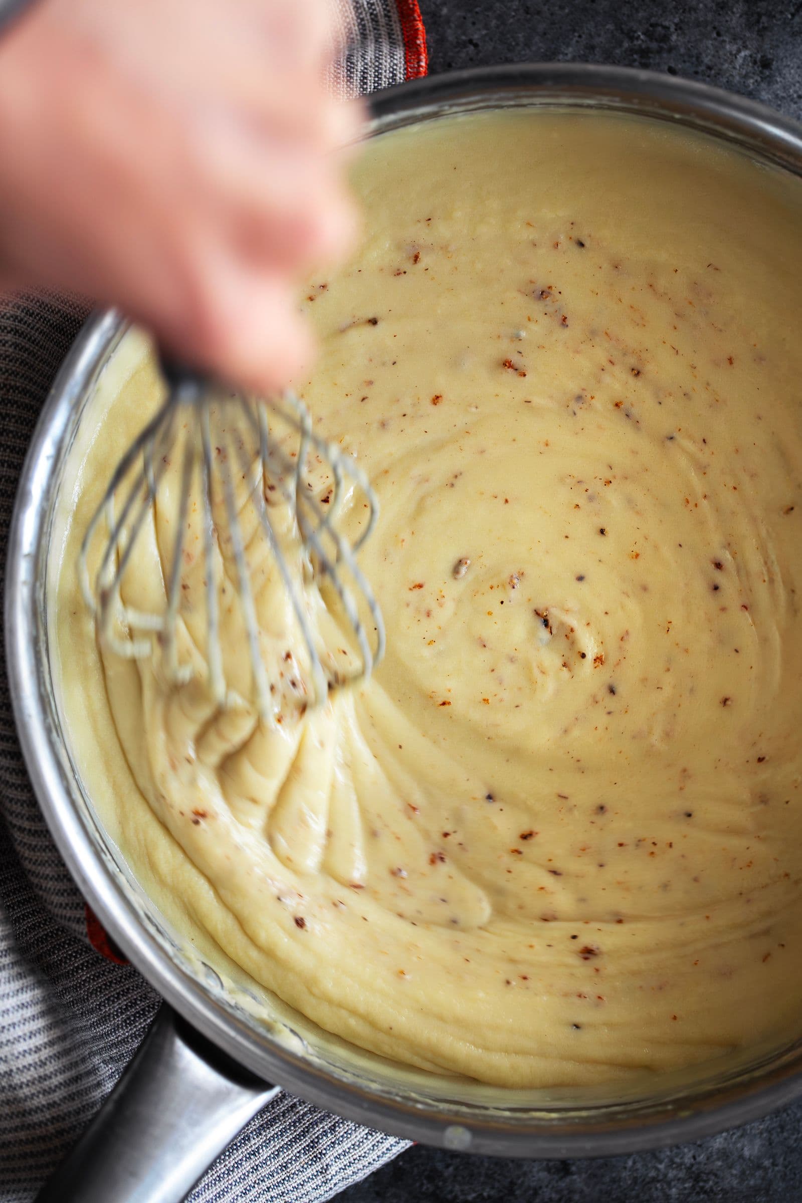 Hand whisking thick vegan béchamel with visible flecks of nutmeg
