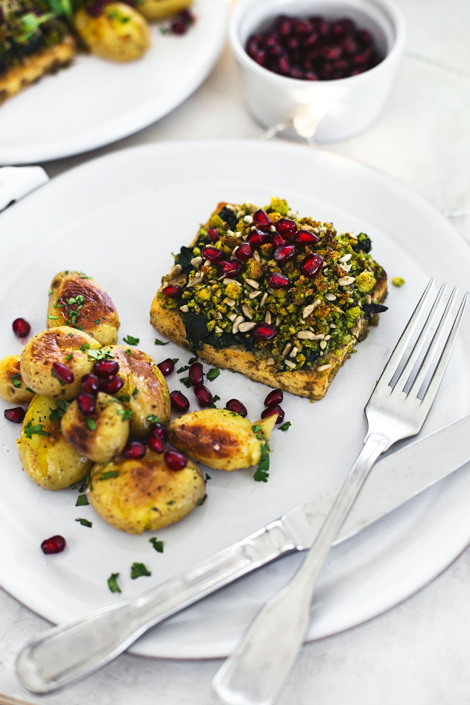 A festive plate with tofu roast topped with cornbread crumble, served with golden roasted potatoes and pomegranate seeds.
