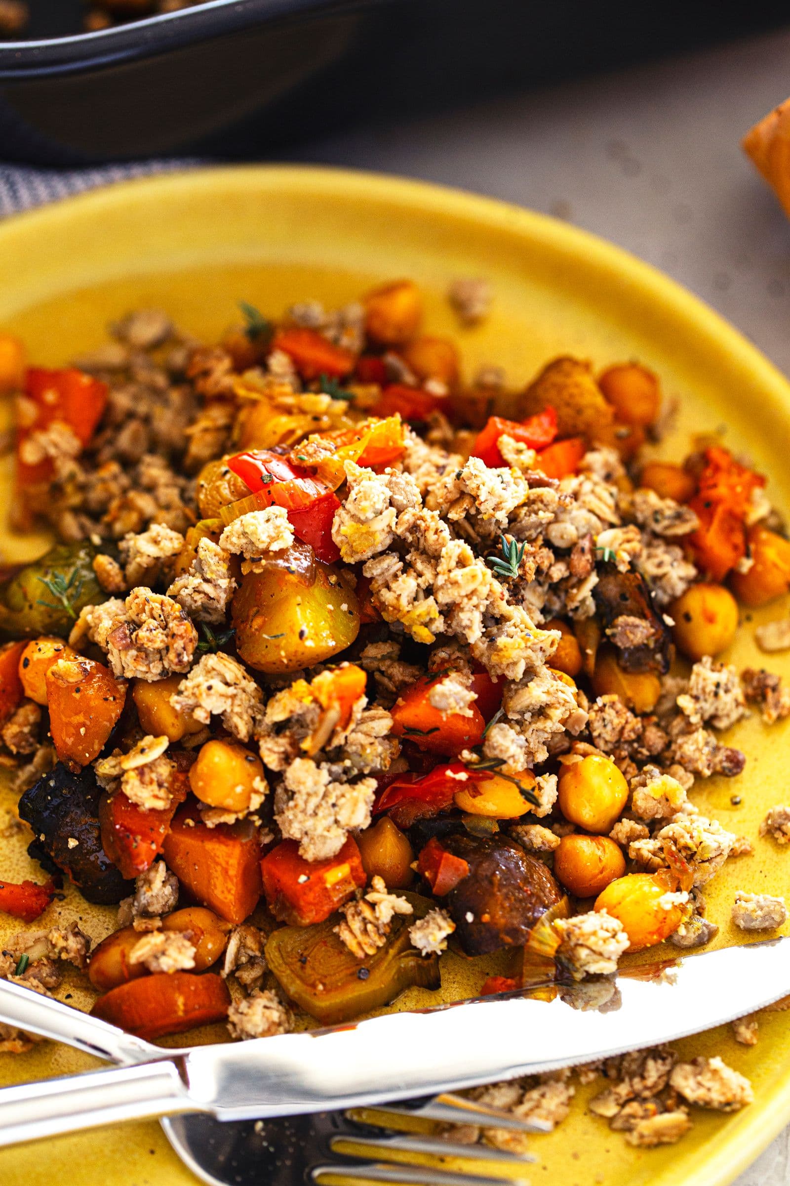 Porção individual de crumble de vegetais no prato, com textura dourada e pedaços de grão-de-bico visíveis.