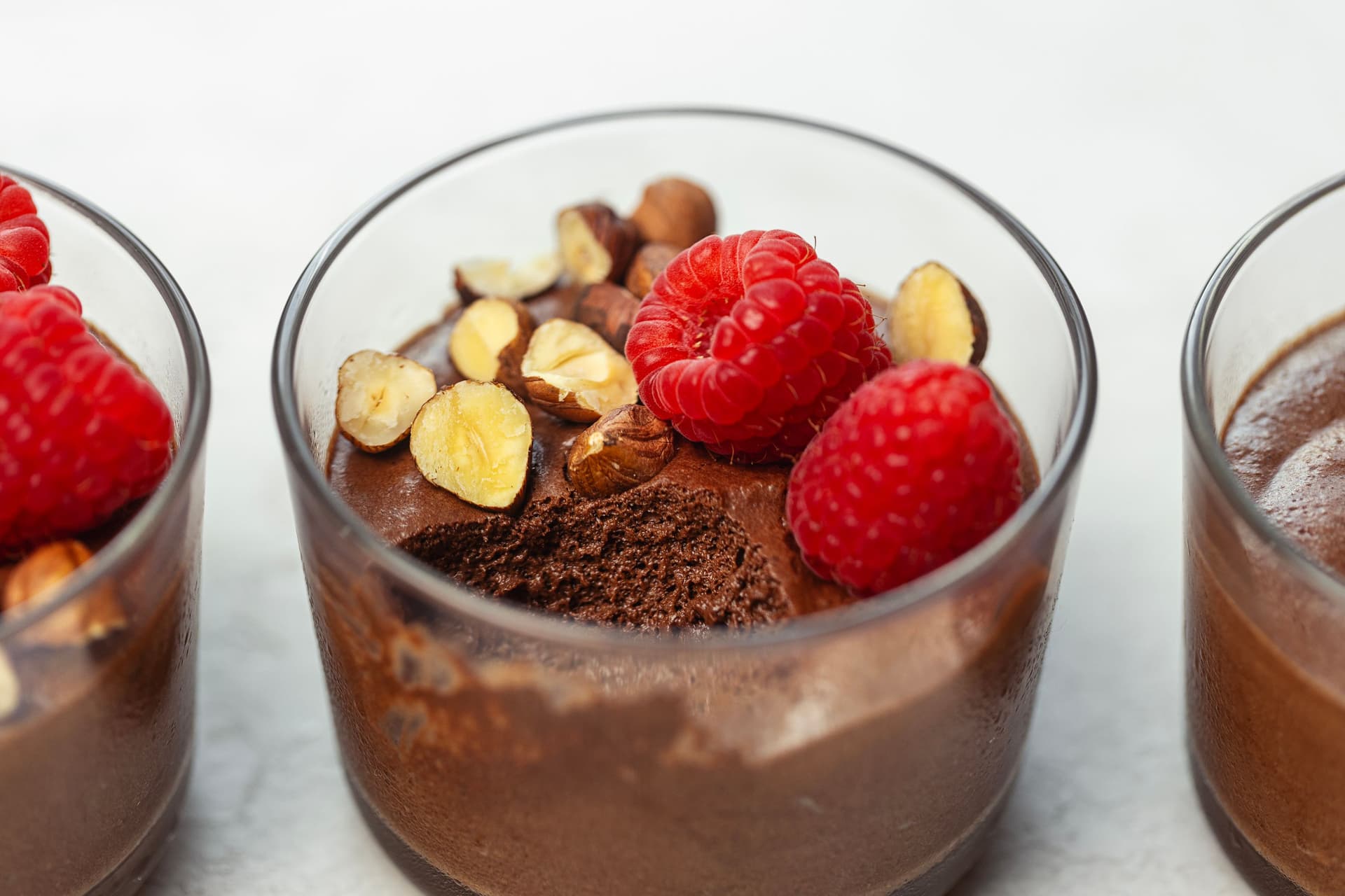 Close-up of vegan chocolate mousse in a glass cup topped with raspberries and nuts.