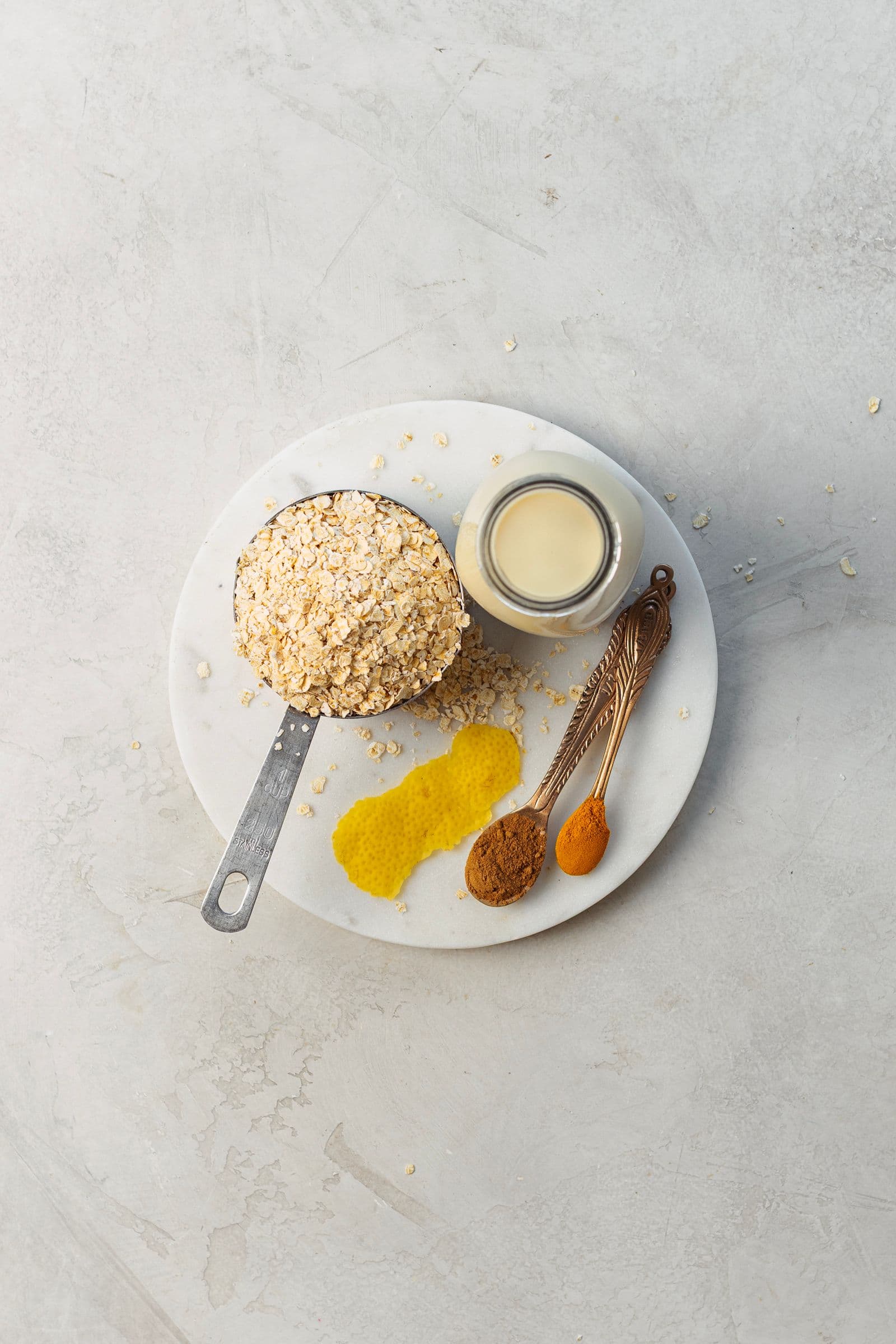 Foto de cima com flocos de aveia, bebida vegetal, casca de limão, canela e curcuma sobre prato branco