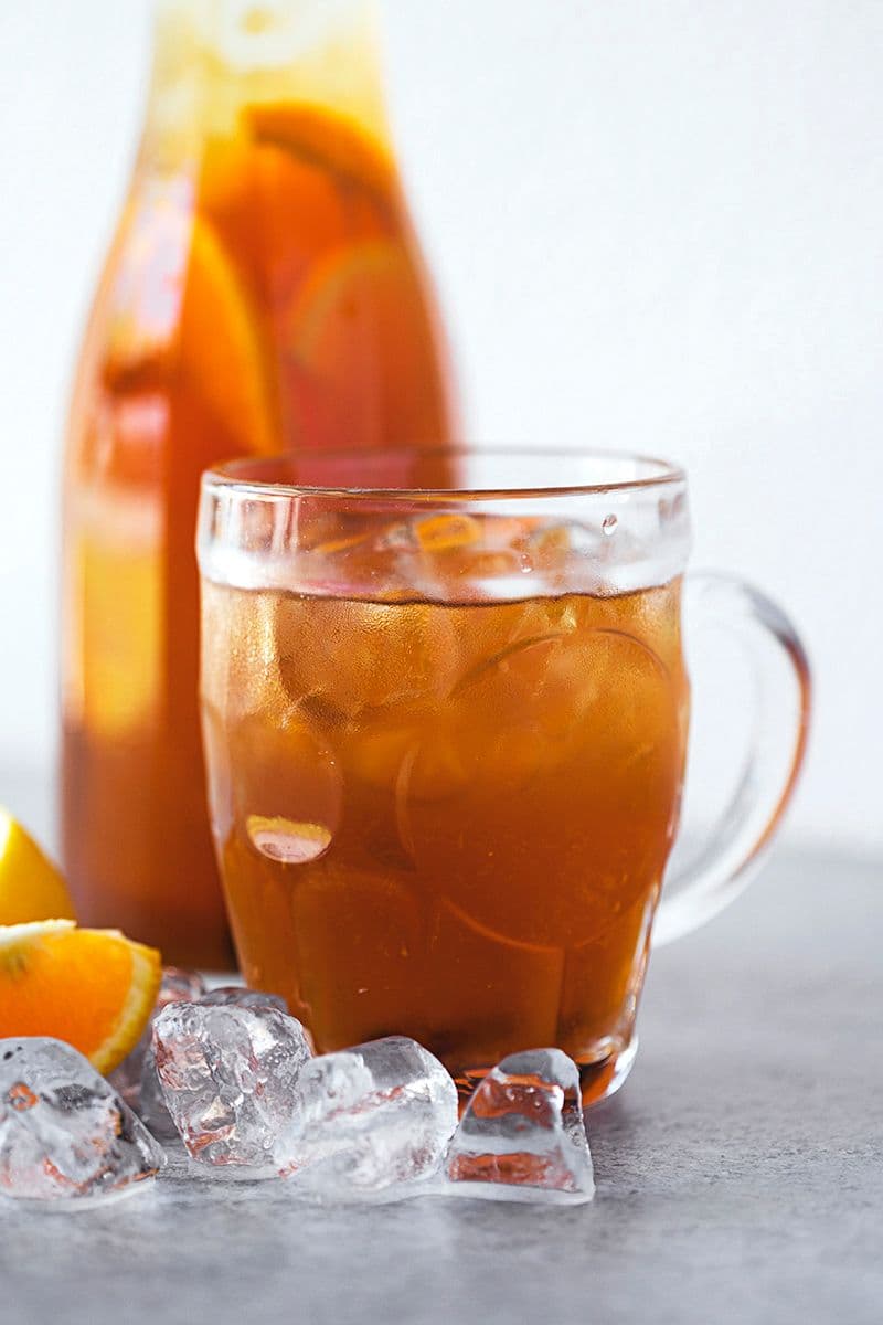 Glass mug of citrus iced tea surrounded by ice cubes, with tea bottle blurred in background.