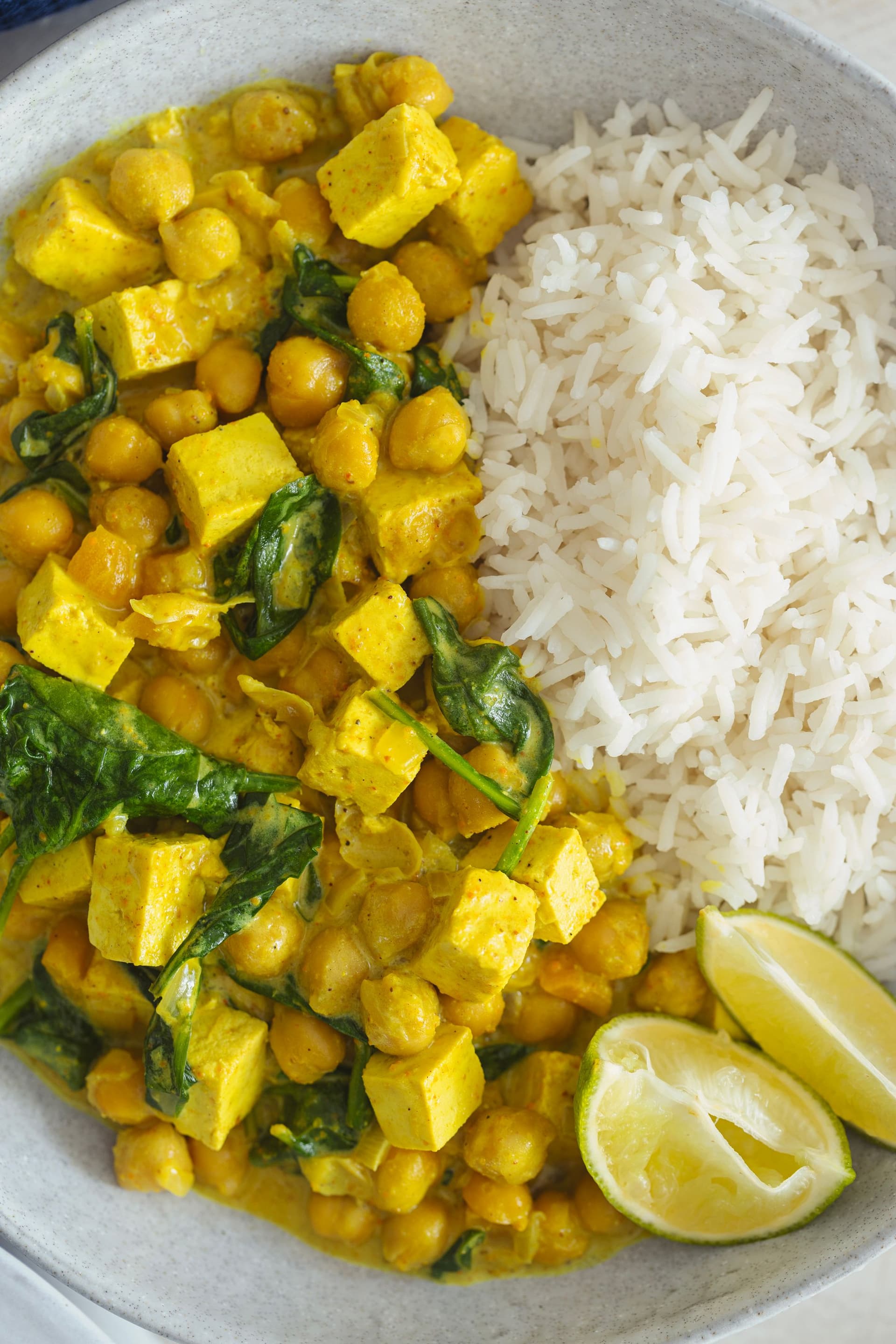 Close-up of curry served with white rice and lemon on a grey ceramic plate.