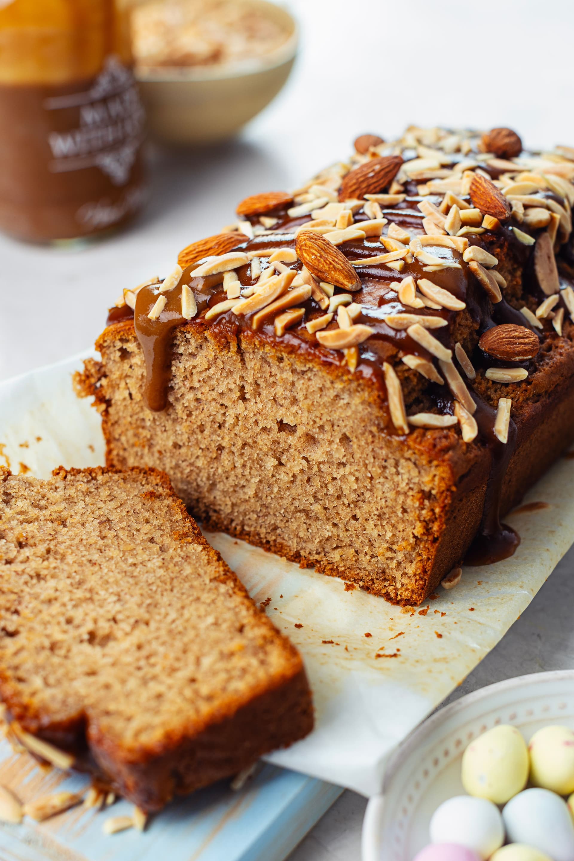 Vegan almond cake cut open with a slice in front revealing the soft interior, topped with caramel and almonds.