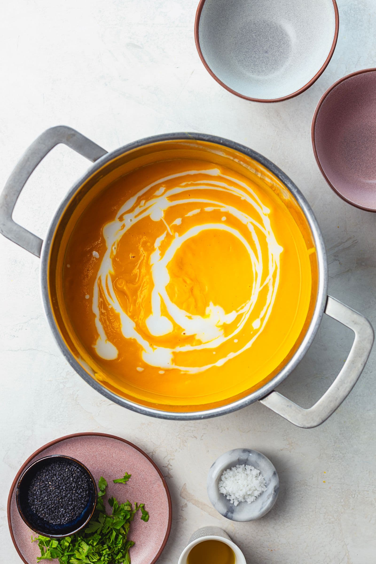 Sopa de cenoura já triturada, lisa e aveludada, com um fio de leite de coco a criar um efeito marmoreado à superfície.