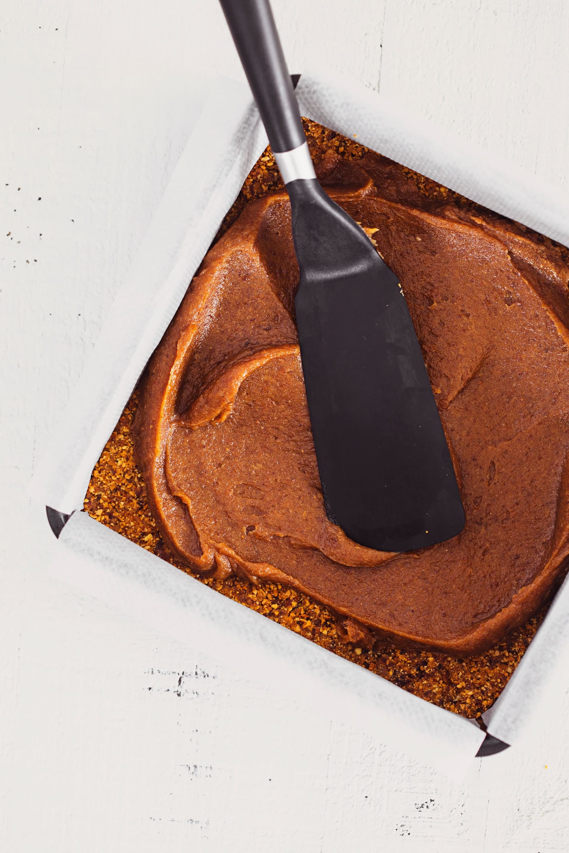 Spatula spreading a thick salted date caramel layer into the tin.